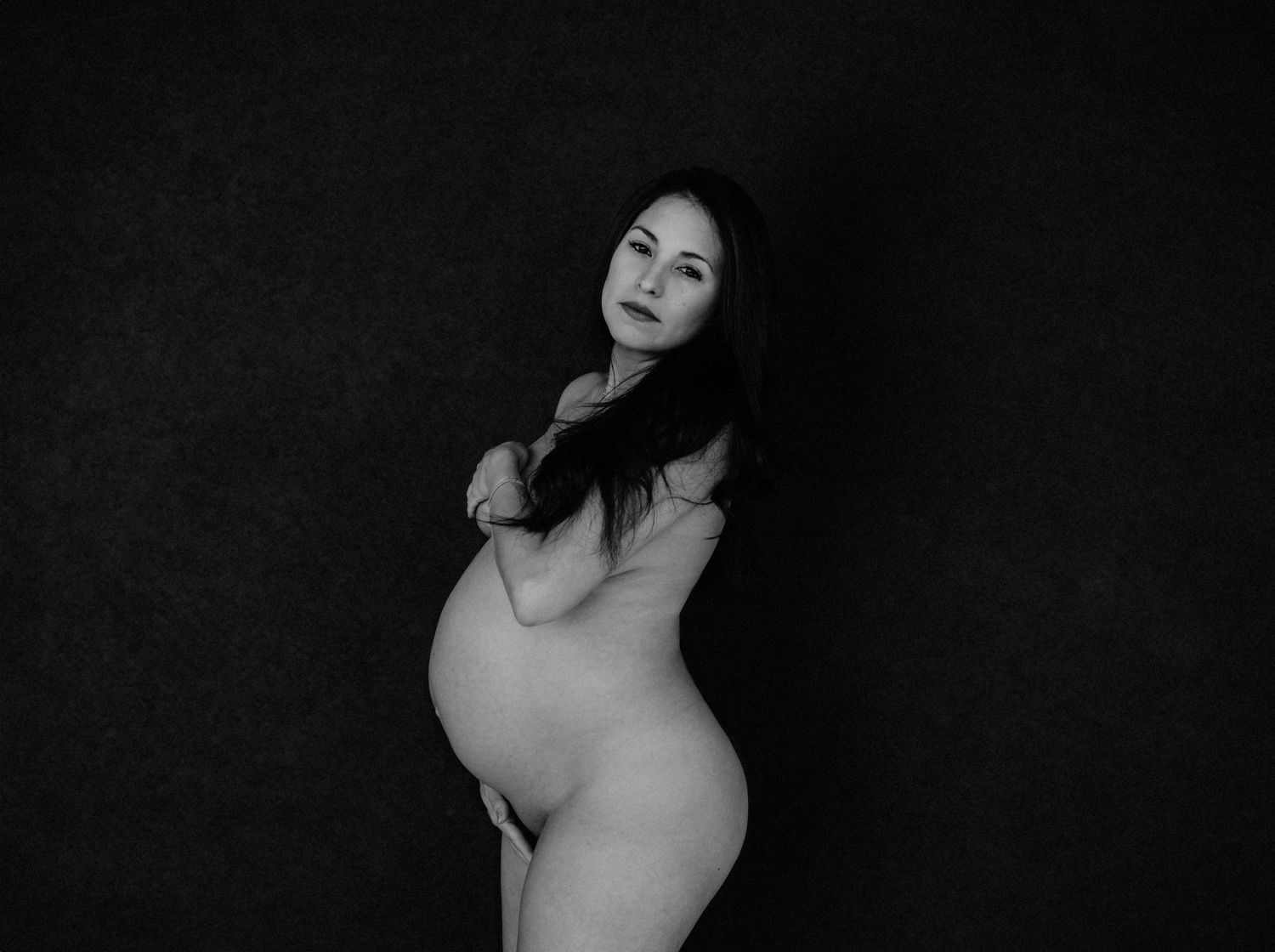 Artistic black and white maternity portrait against dark backdrop.