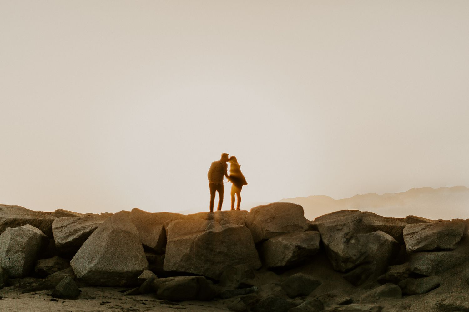 Silhouette of couple standing on rocks at sunset creates dramatic romantic scene.