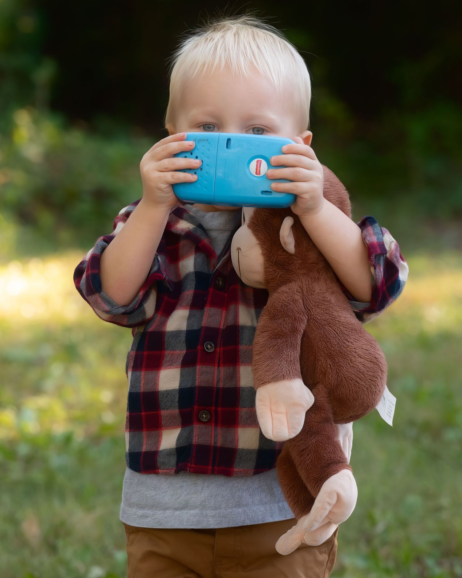 Little hands holding a toy cell phone to capture a photo — intimate outdoor portrait in the Missouri countryside.