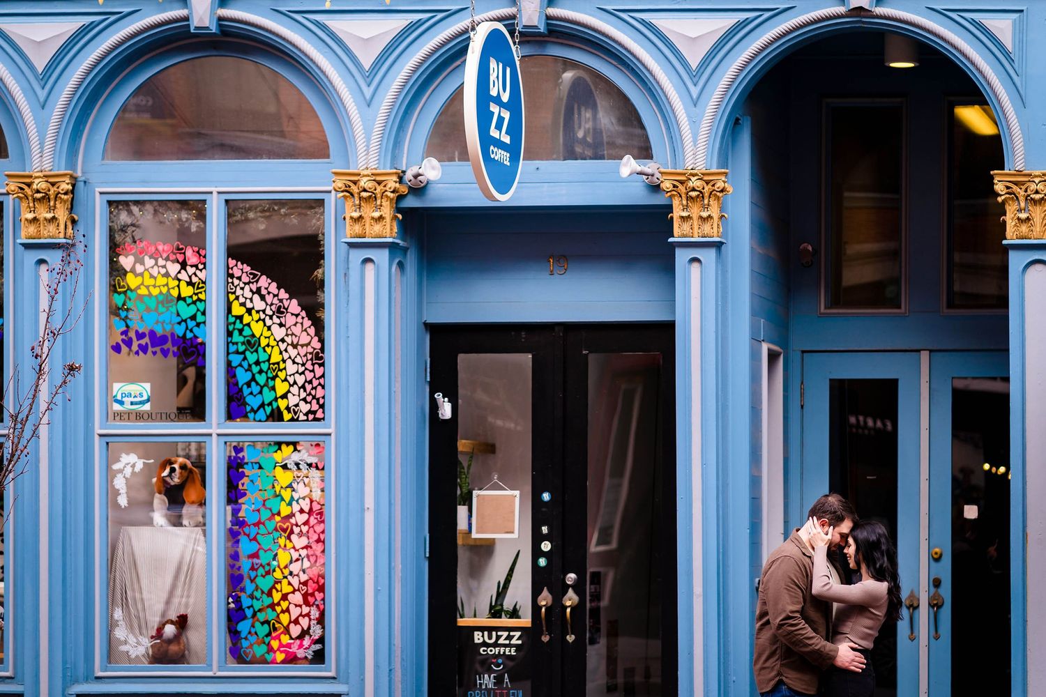 A blue storefront with arched windows featuring a colorful rainbow balloon display.