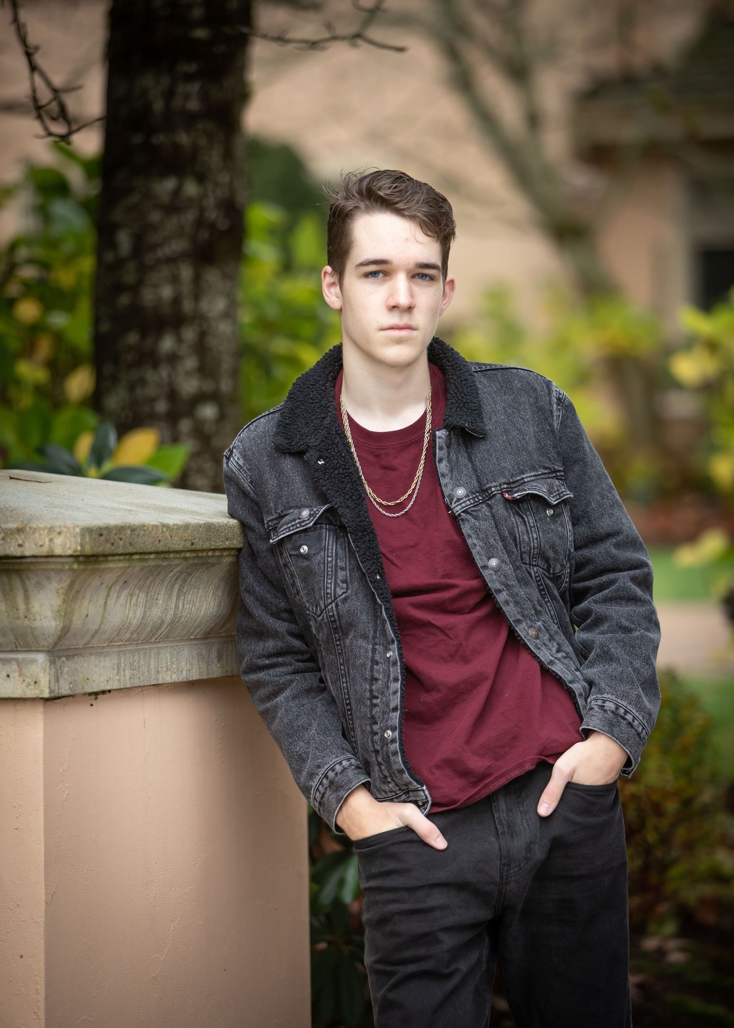 High school boy leaning against a concrete pillar with his hands in his pockets