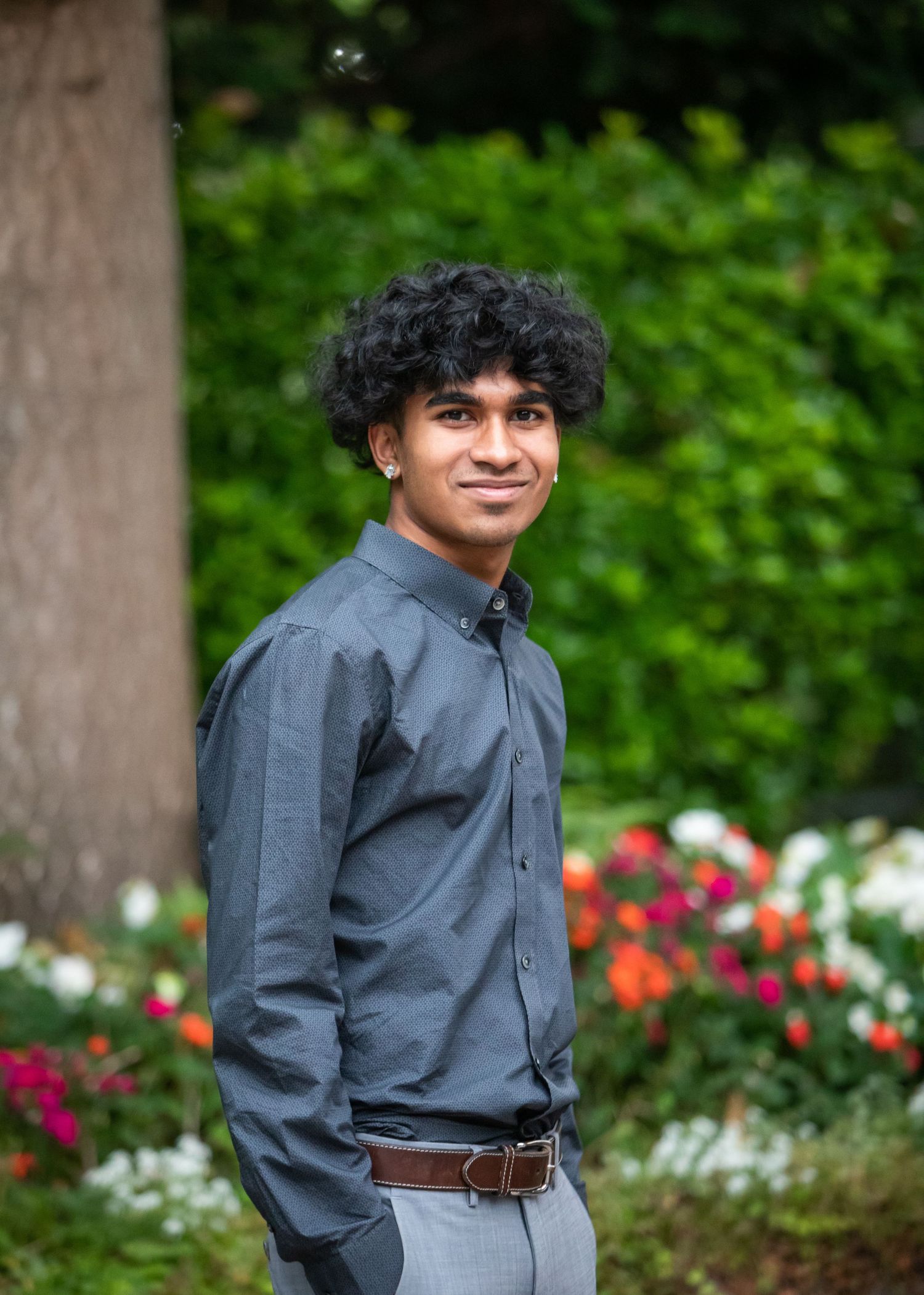 High school boy posed casually in front of green shrubs and colorful flowers
