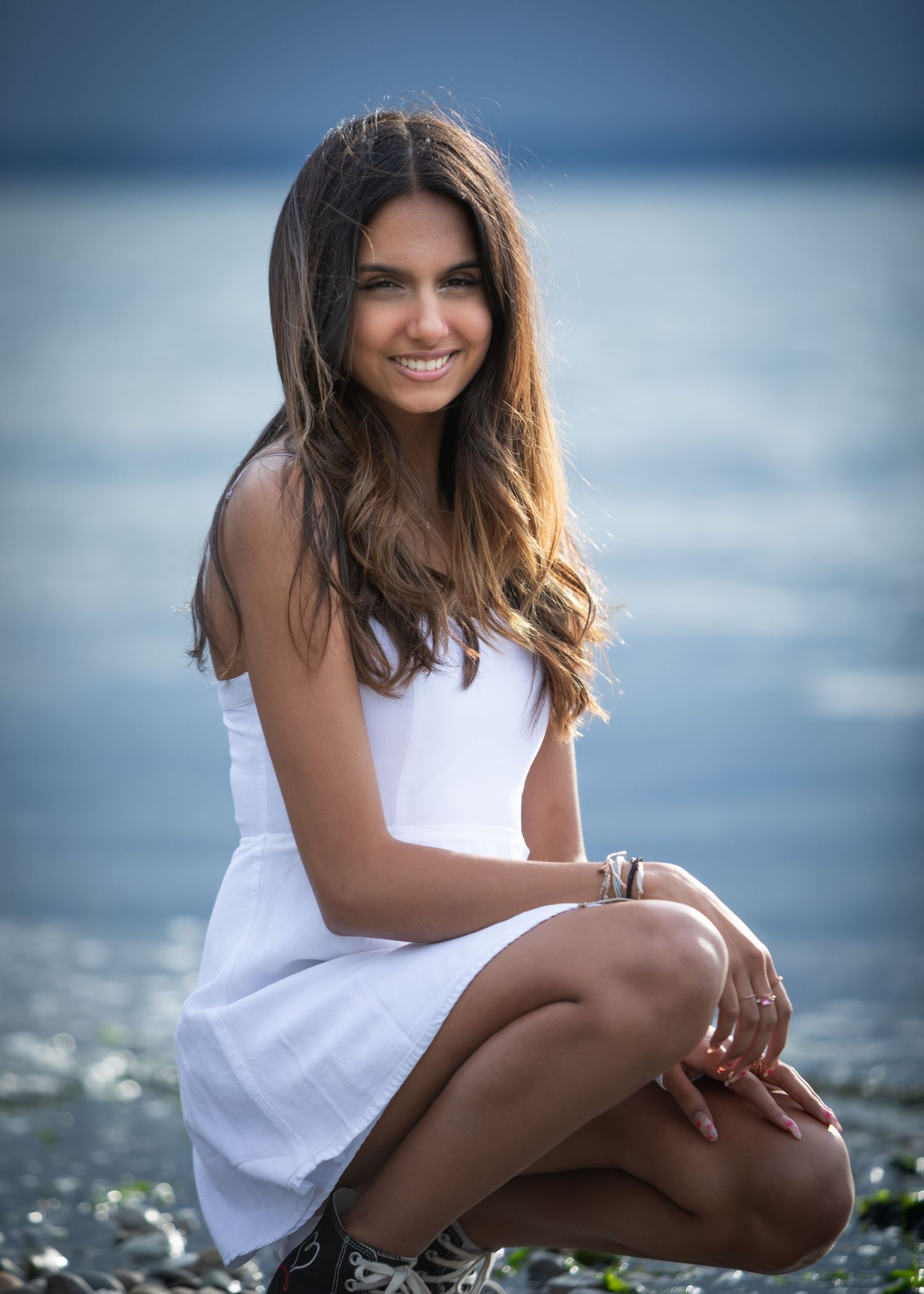 High school girl in a short white dress kneeling at the beach