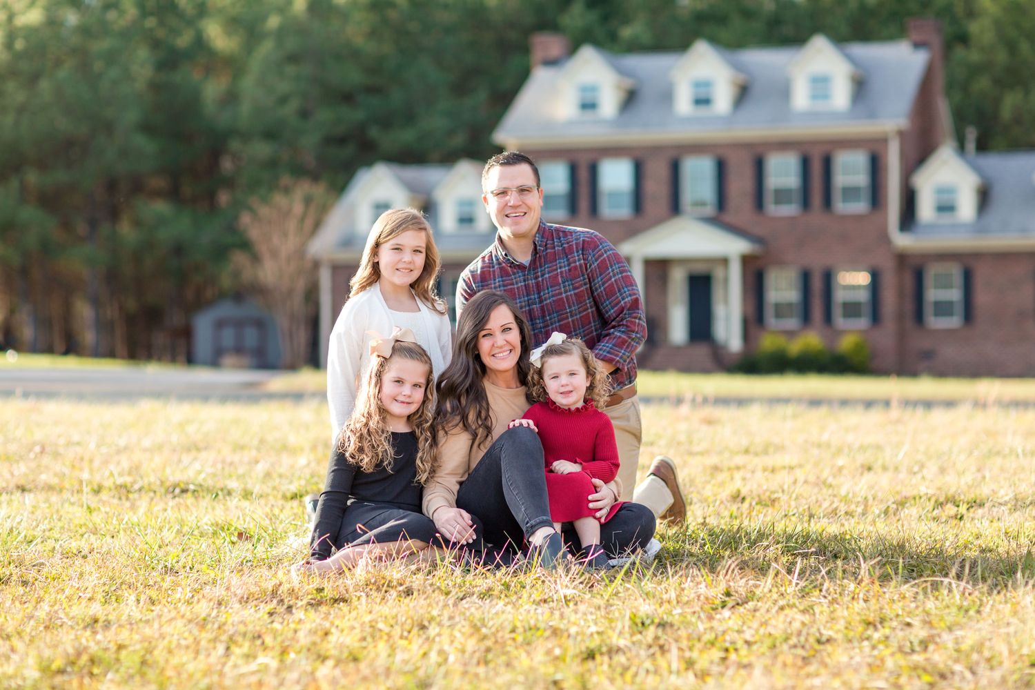 family portrait of mom, dad and 3 daughters sitting in a field in front of their house