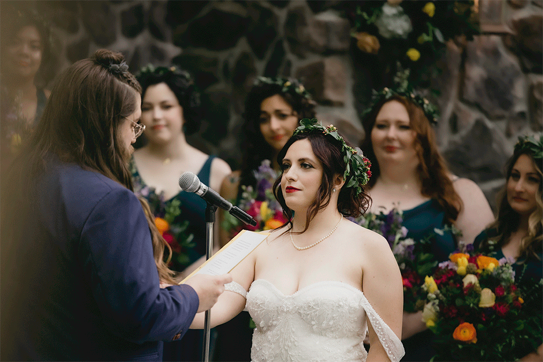Outdoor wedding ceremony with bride and attendants surrounded by colorful flowers.