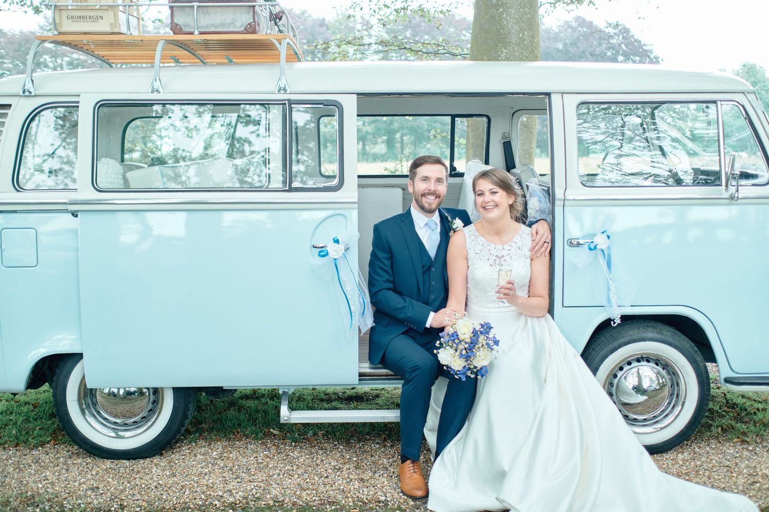 Newlyweds pose beside classic light blue Volkswagen van on their wedding day.