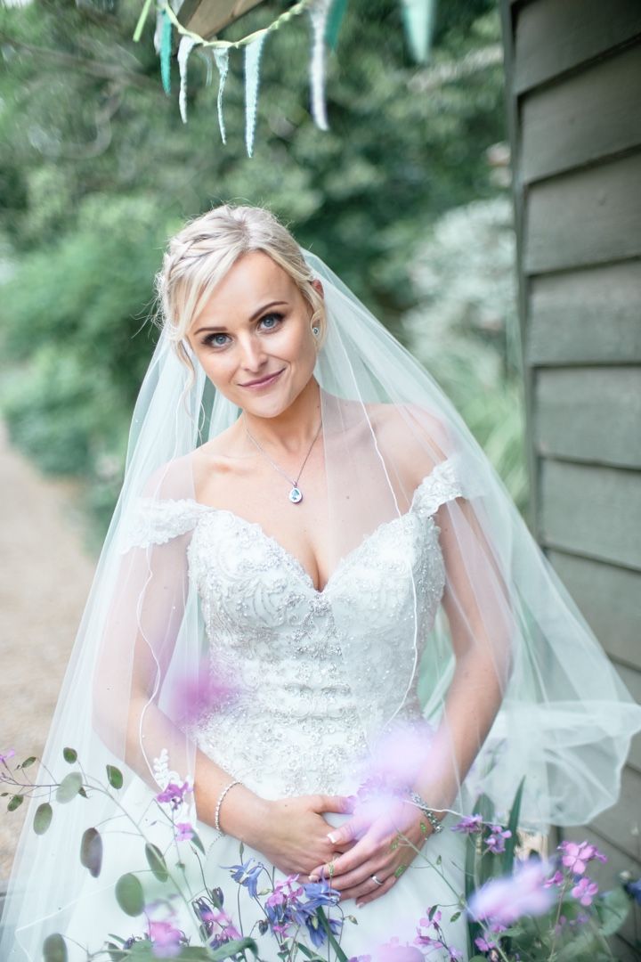 A bride in white lace gown poses with flowers and icicle decorations in a garden setting.