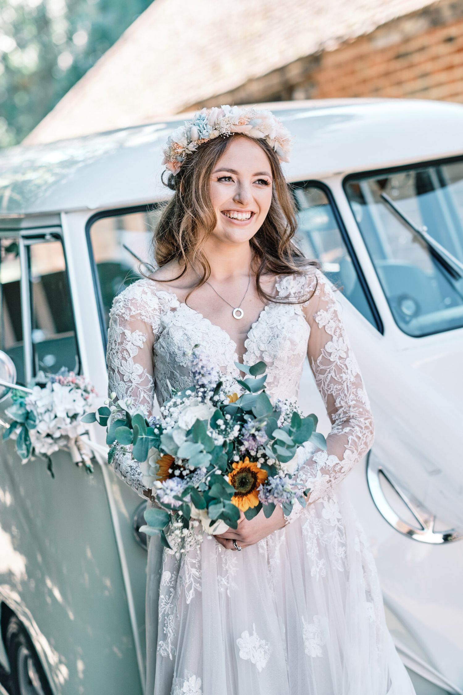 A bride in a lace wedding dress poses with a sunflower bouquet next to a vintage white van.