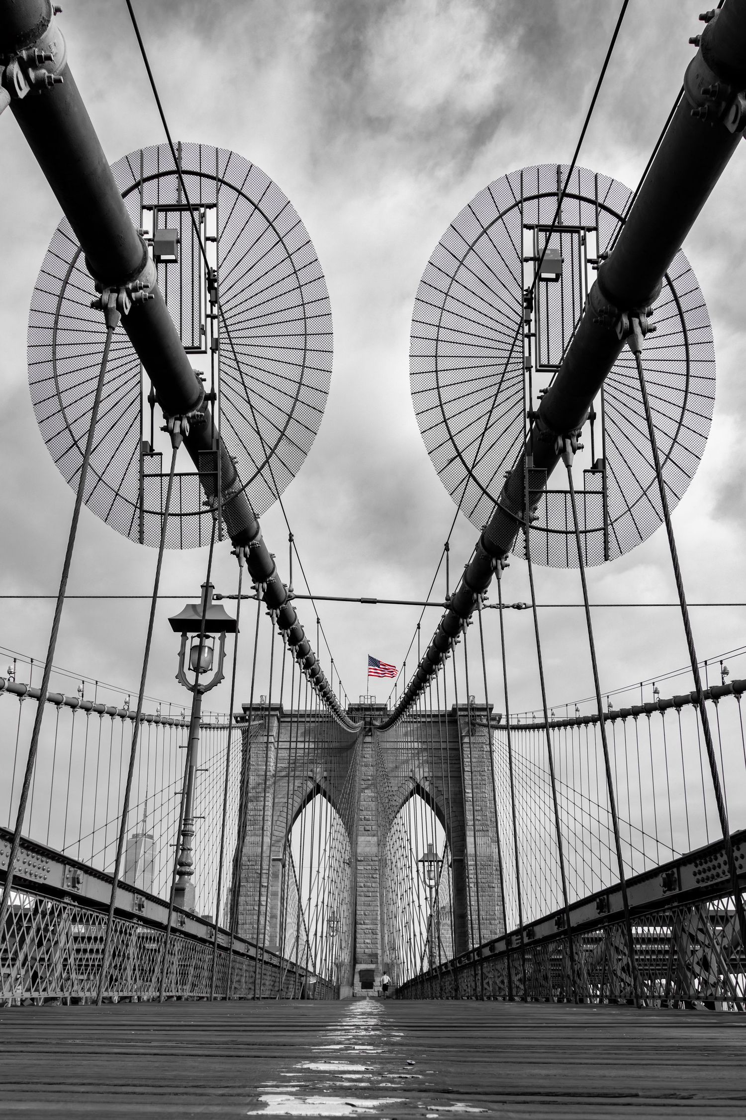 jogger on Brooklyn Bridge New York looking over to Manhattan and One World Trade Center in black and white with US flag 