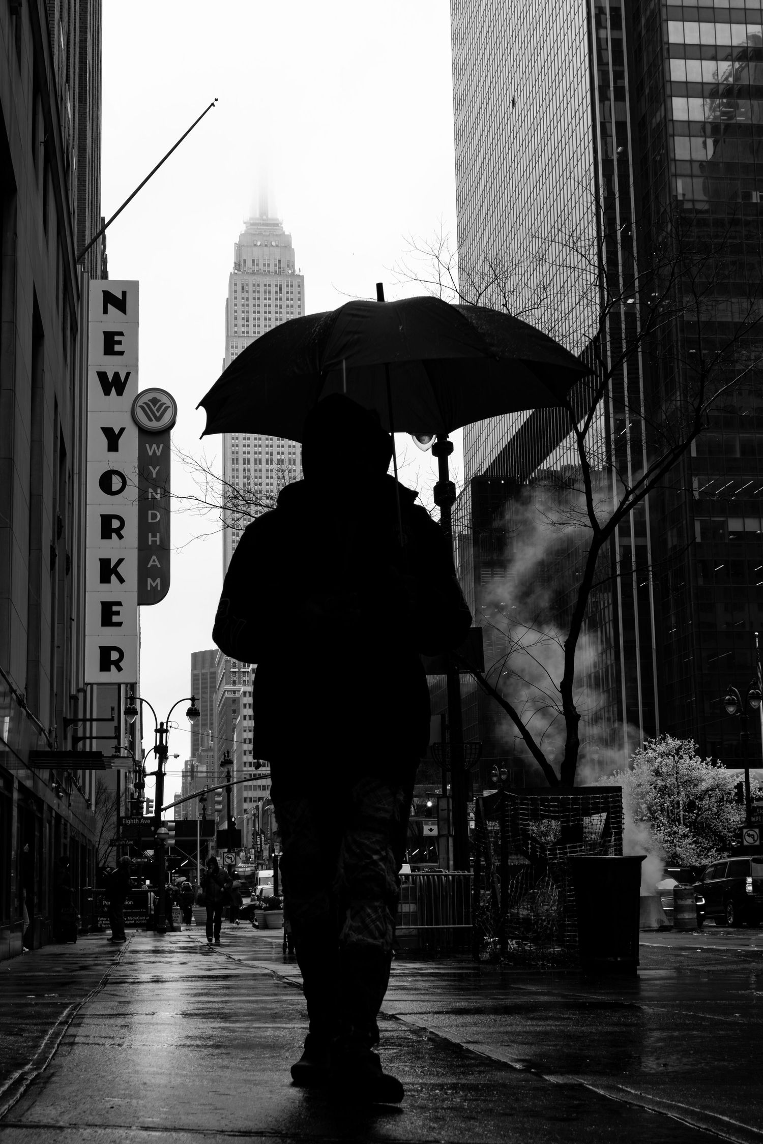 Black and white photo on a rainy day in New York City looking towards The Empire State Building and New Yorker hotel by 