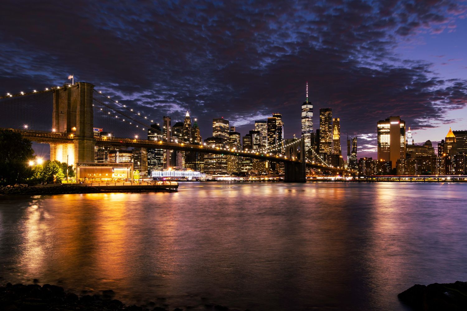 The Brooklyn Bridge at night connecting Brooklyn and Manhattan with One World Trade Center by Kush Rattan Photography