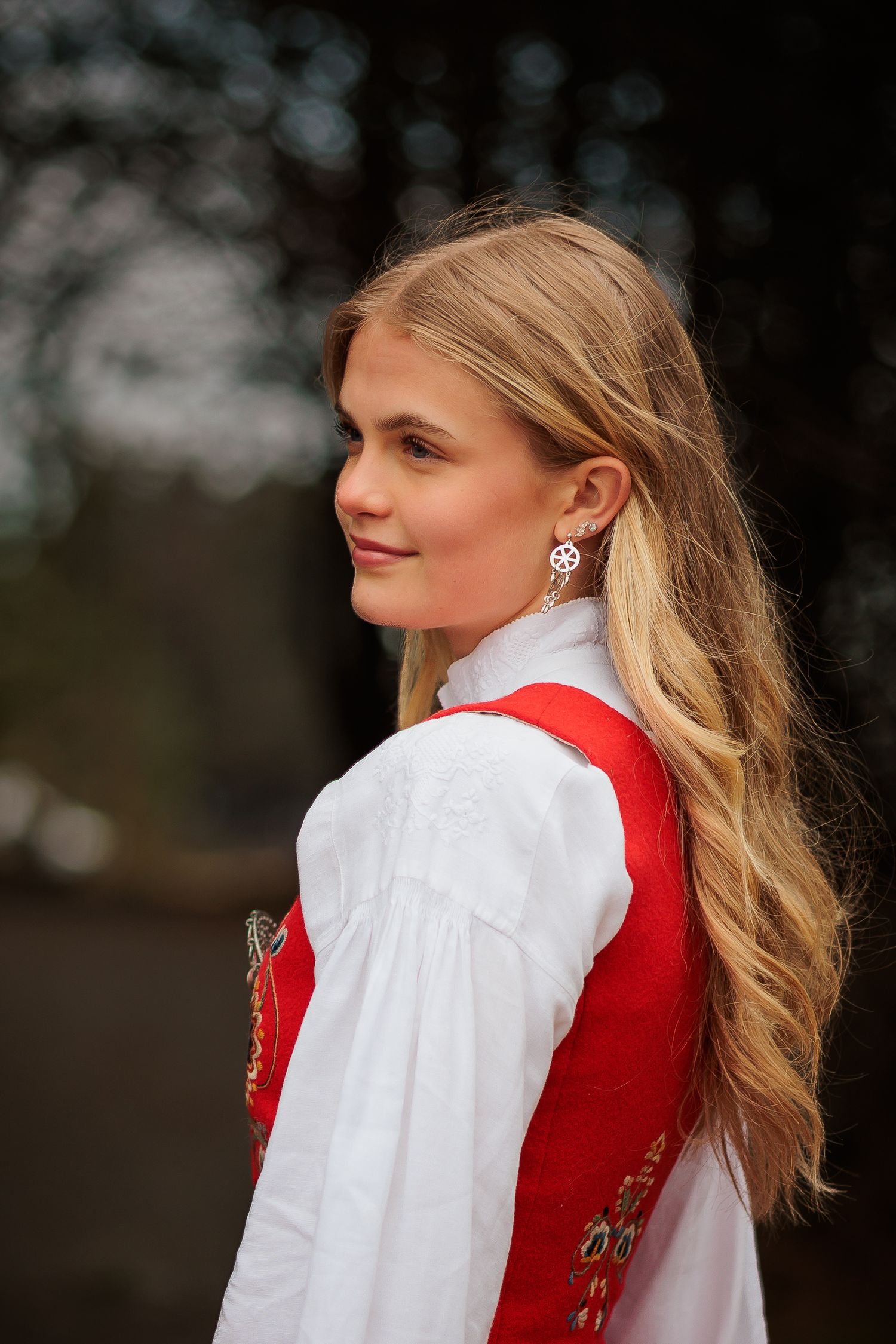 Portrait featuring traditional Norwegian folk costume with white blouse and red vest against nature backdrop.