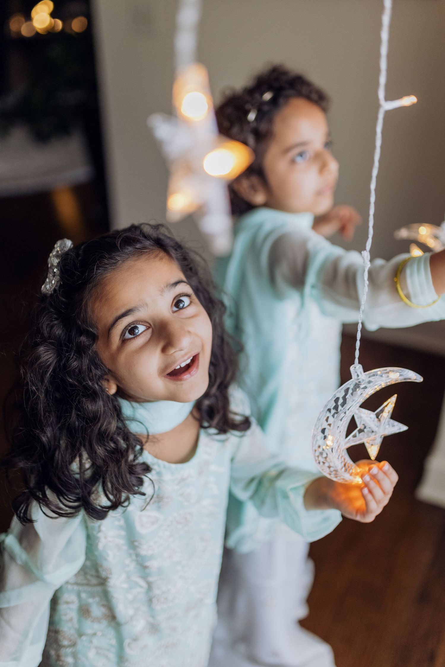A young girl smiles in fascination in traditional desi clothing during Ramadan while holding a crescent moon light decor