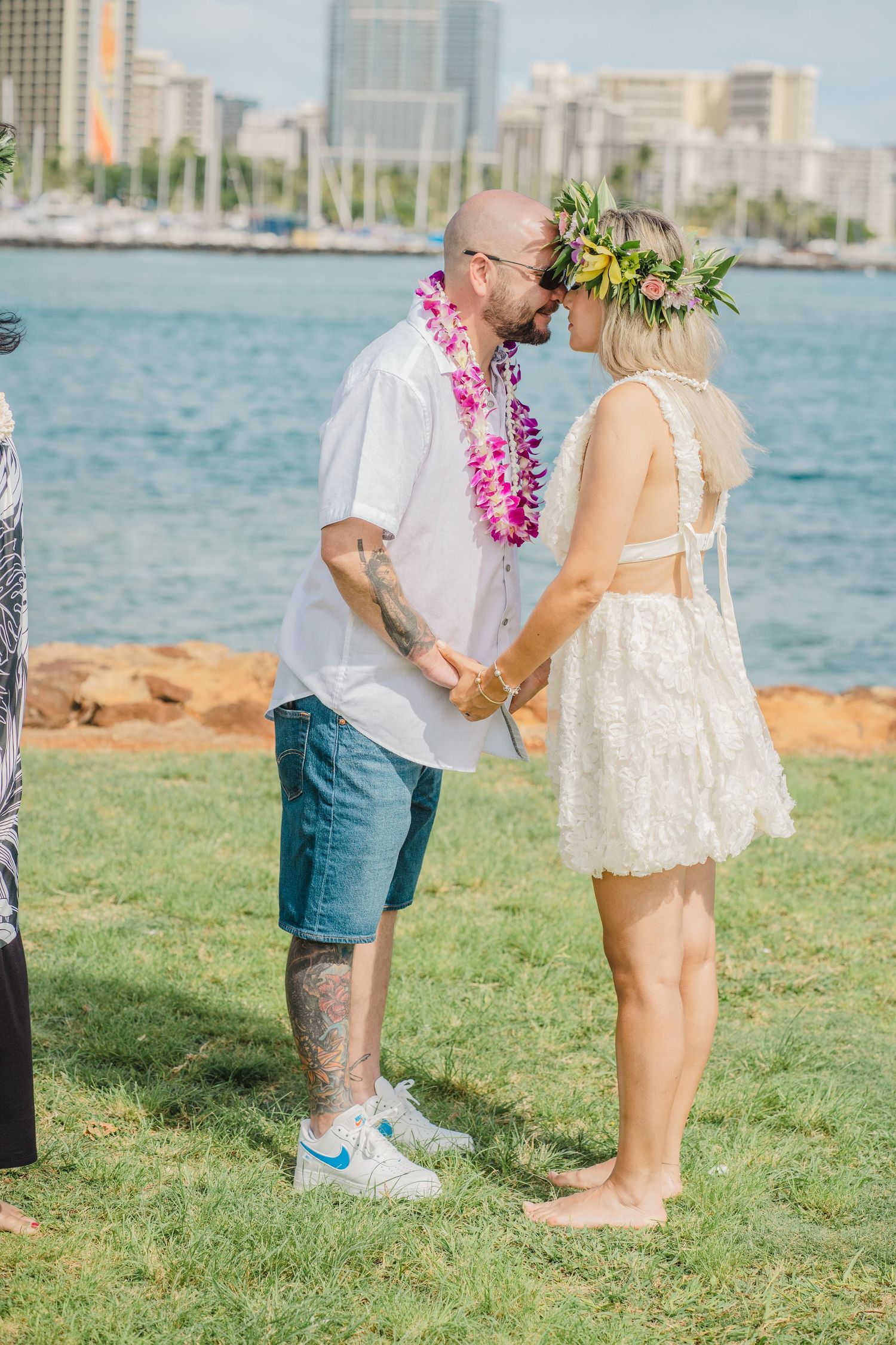 Beach wedding ceremony with lei-adorned couple against Honolulu harbor backdrop.