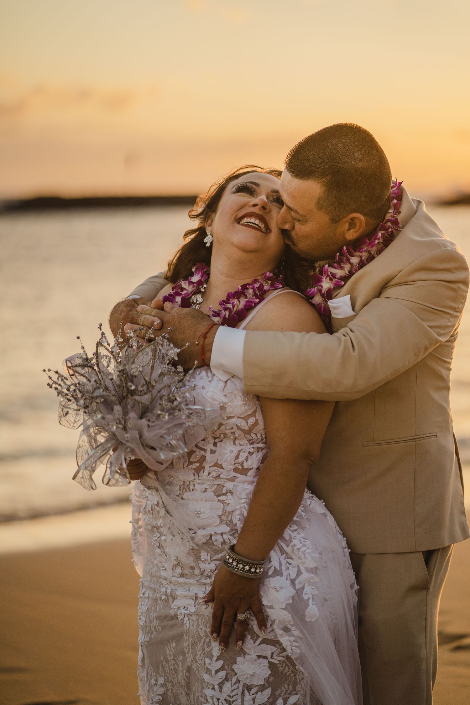 Sunset beach wedding portrait with couple wearing Hawaiian leis and embracing.