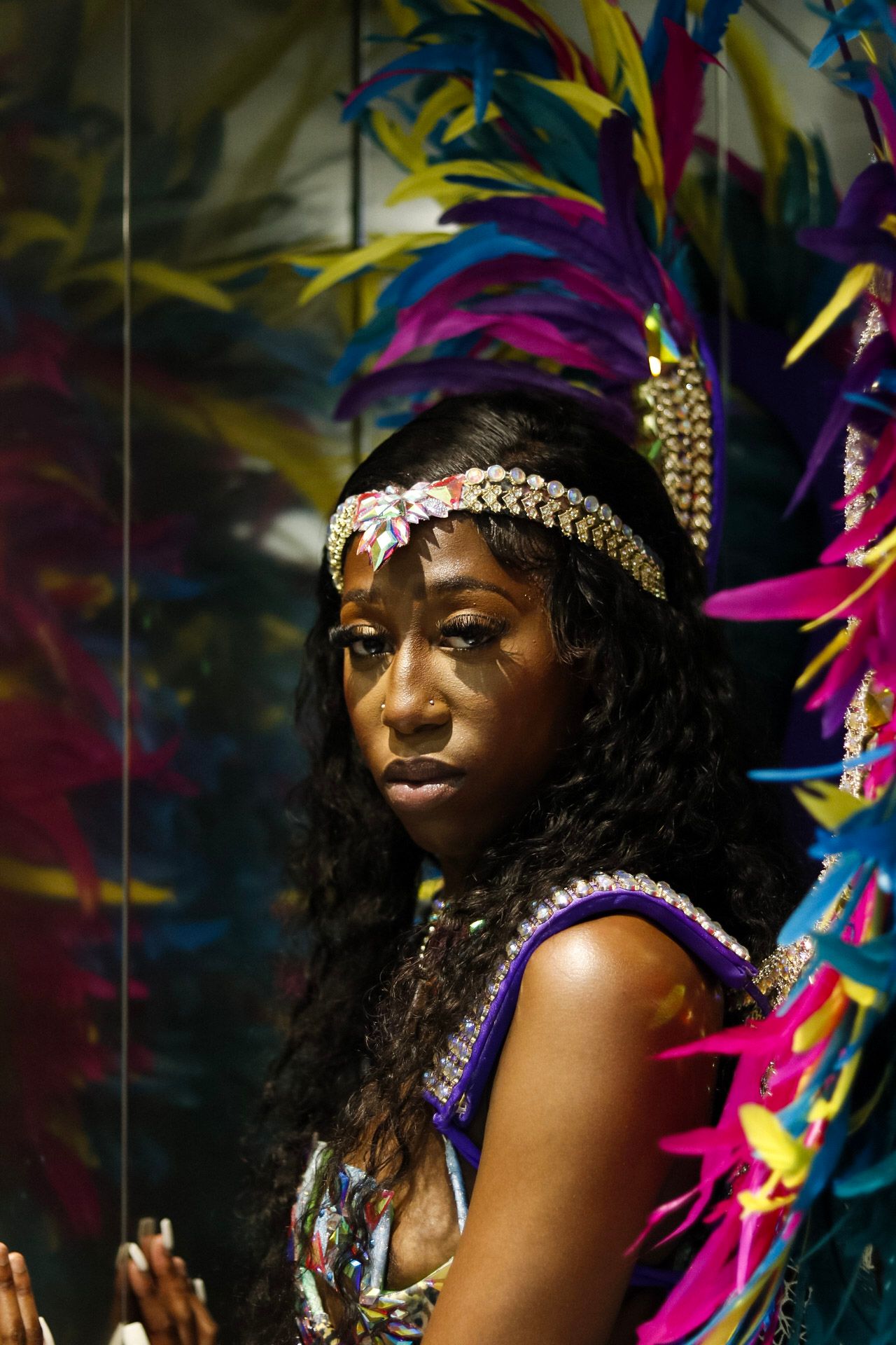 Colorful carnival headdress with bright feathers and jeweled details against dark background.