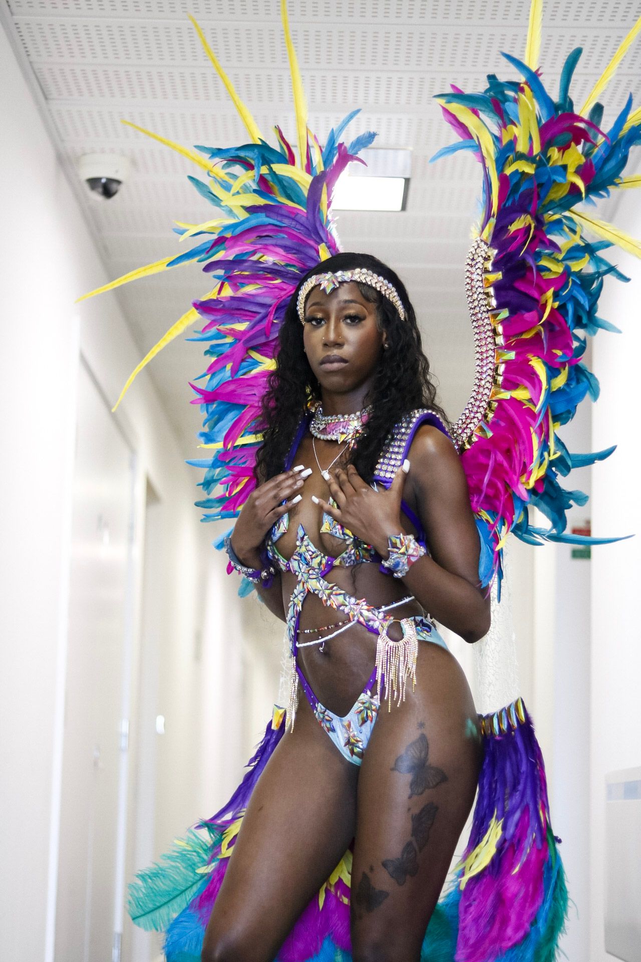 Carnival performer in bright feathered costume photographed against white studio backdrop.