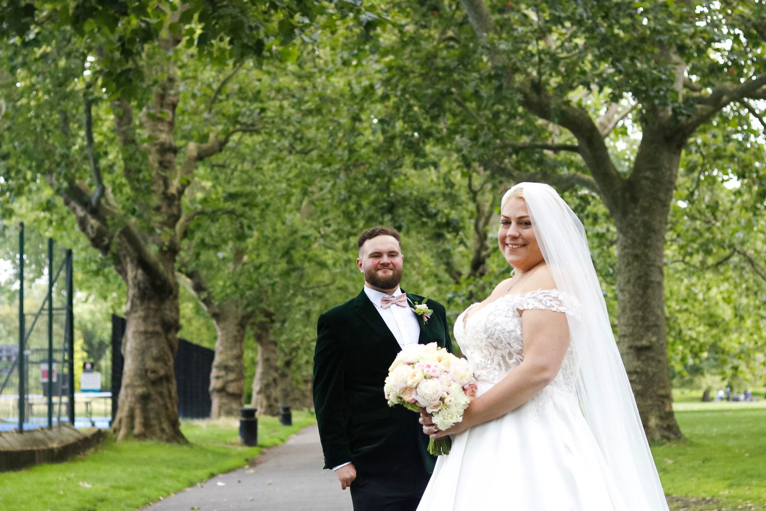 A spring wedding portrait in a tree-lined park with blooming greenery.