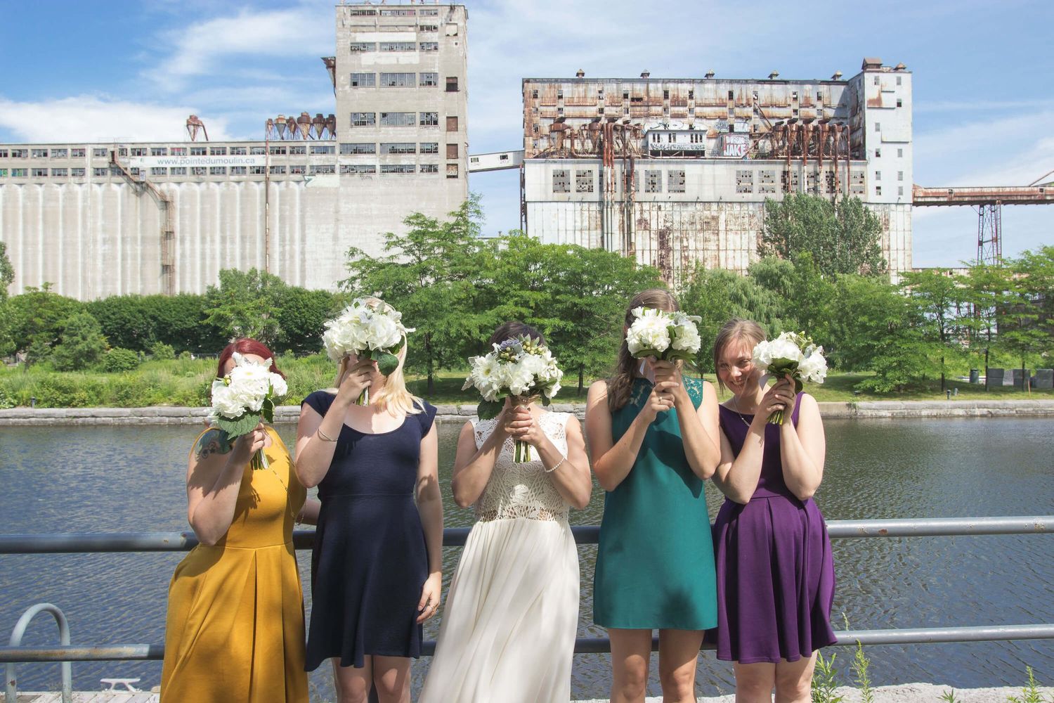 Une mariée et ses filles d'honneur mettent leur bouquet de fleurs devant leur visage, dans le vieux-montréal devant le Silo numéro 5.