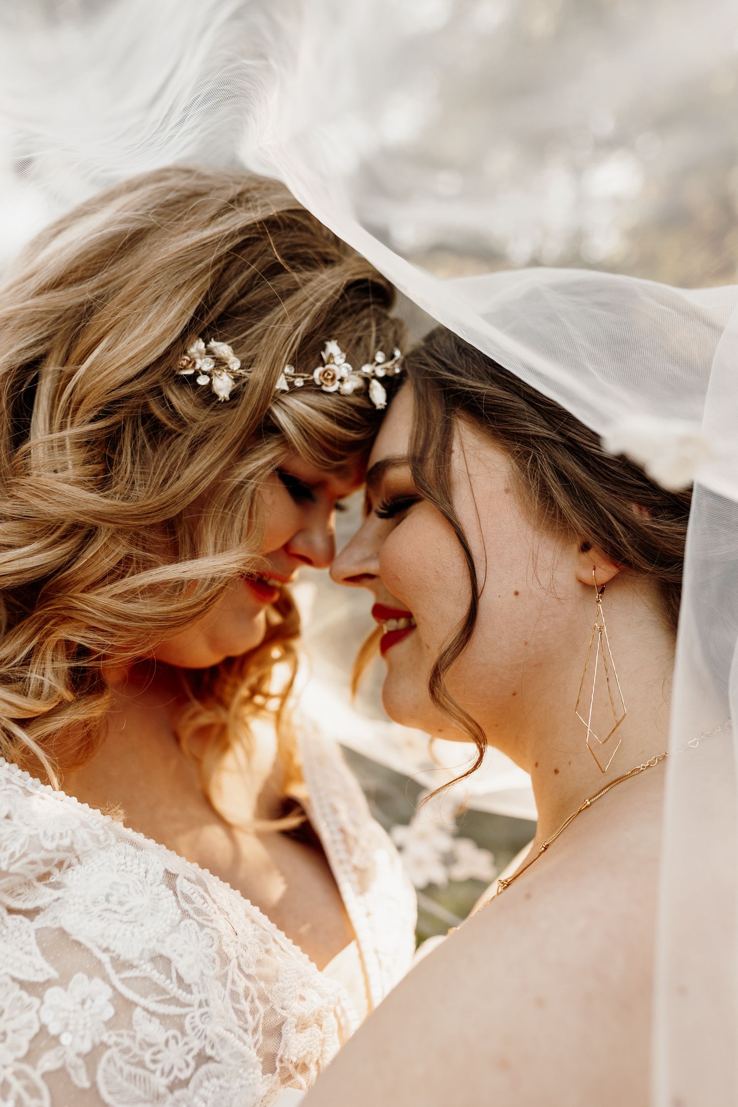 Close-up of two brides sharing intimate moment under wedding veils.