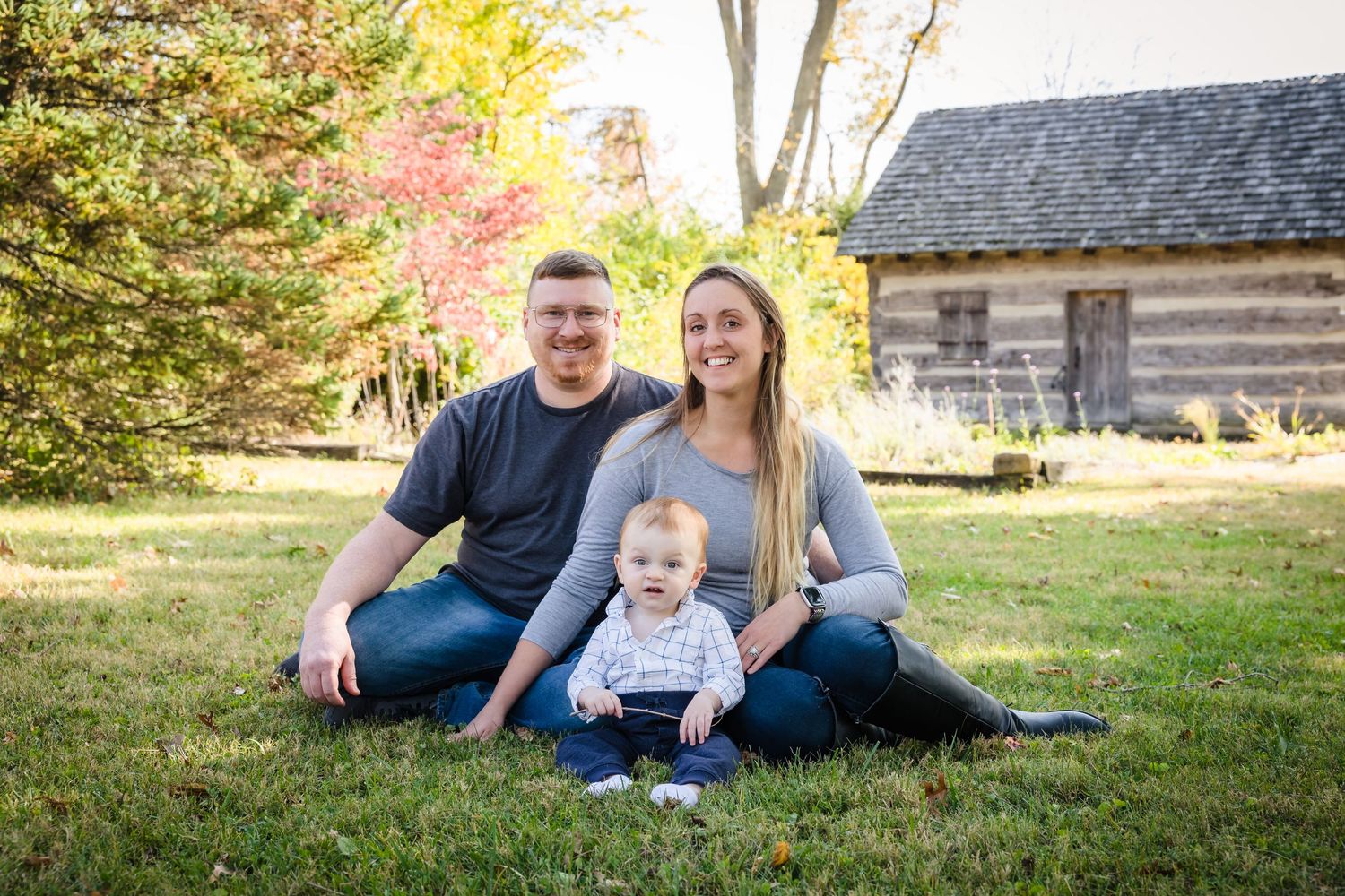 Family portrait session on grass with rustic log cabin in background during autumn.