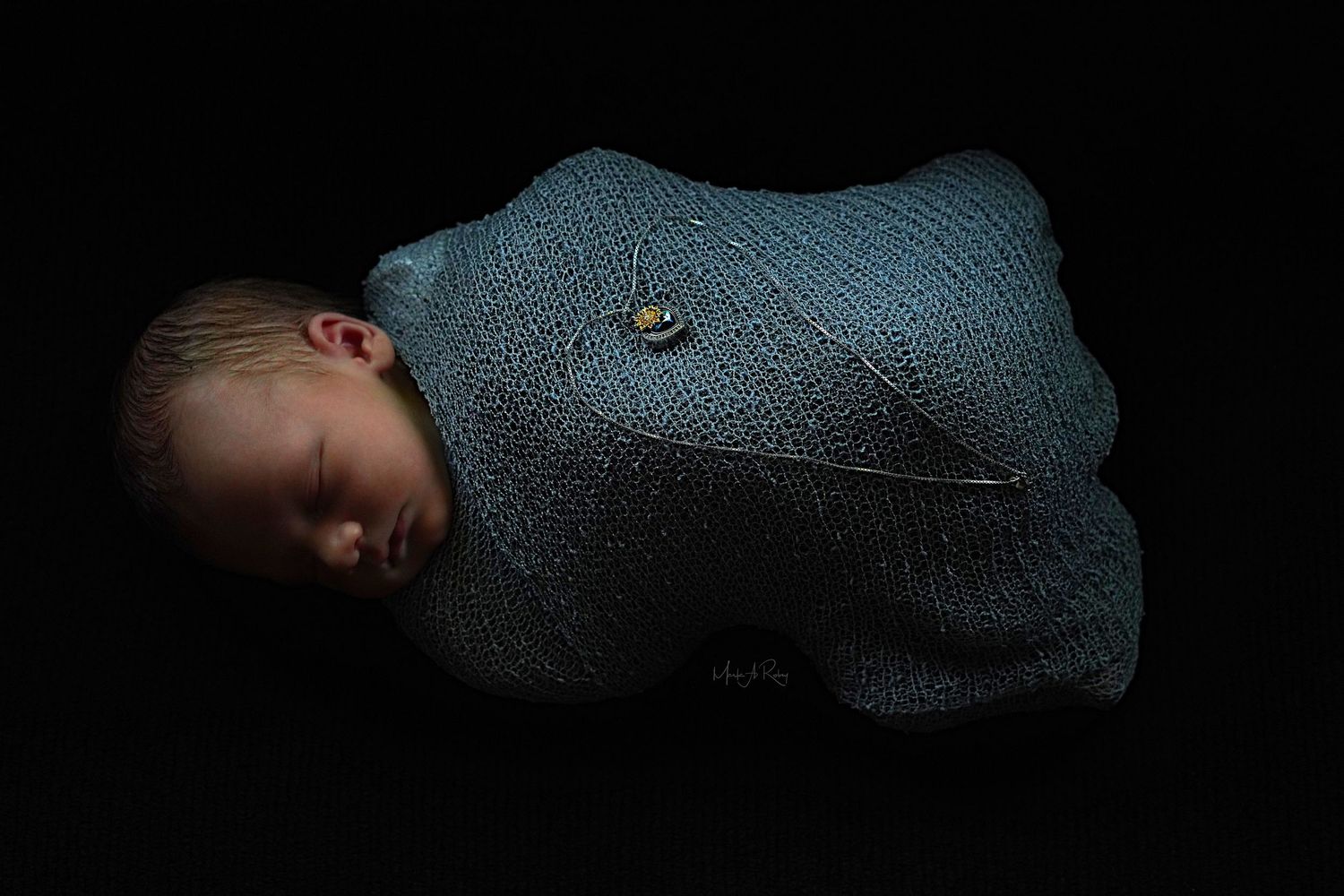 Artistic black and white photo of a sleeping infant wrapped in textured fabric.