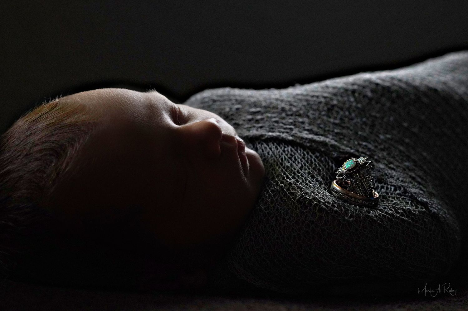 Minimalist newborn portrait with baby wrapped in textured gray fabric against dark background.