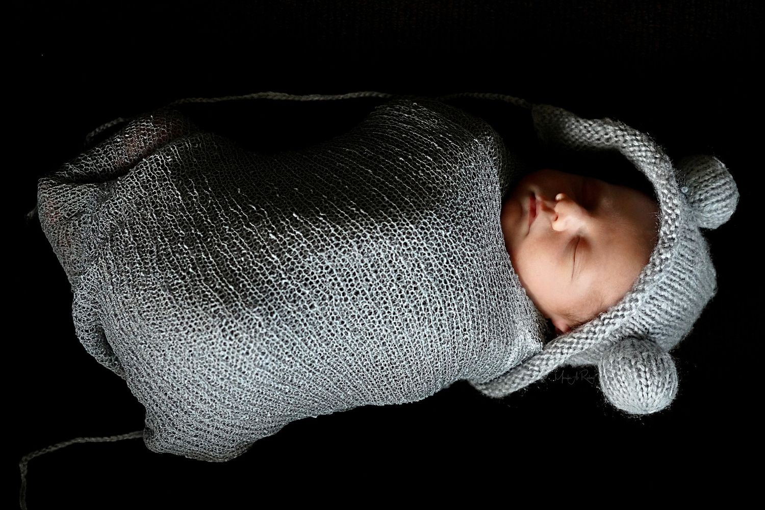 Side profile of newborn baby sleeping peacefully in soft gray swaddle.
