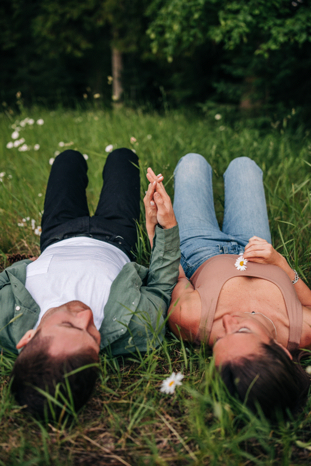A couple relaxes in a meadow holding hands among scattered wildflowers.