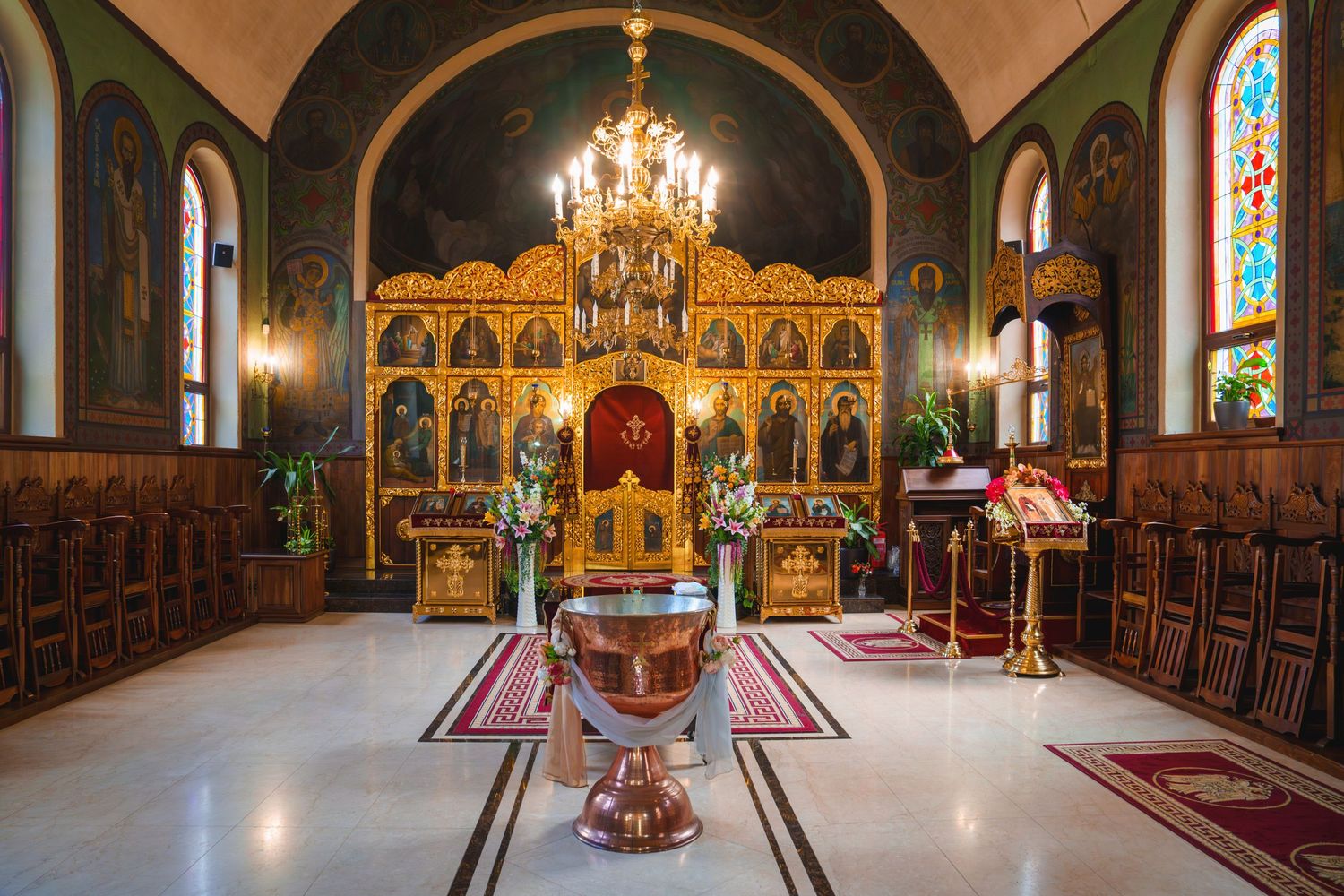 Orthodox church interior with golden iconostasis, chandelier and baptismal font.