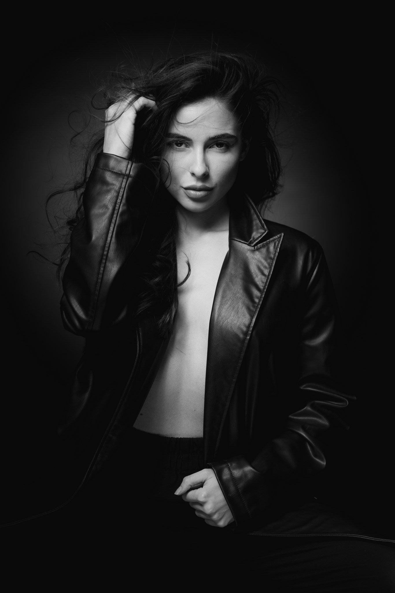 Dramatic black and white portrait of a person in a leather jacket against dark background.