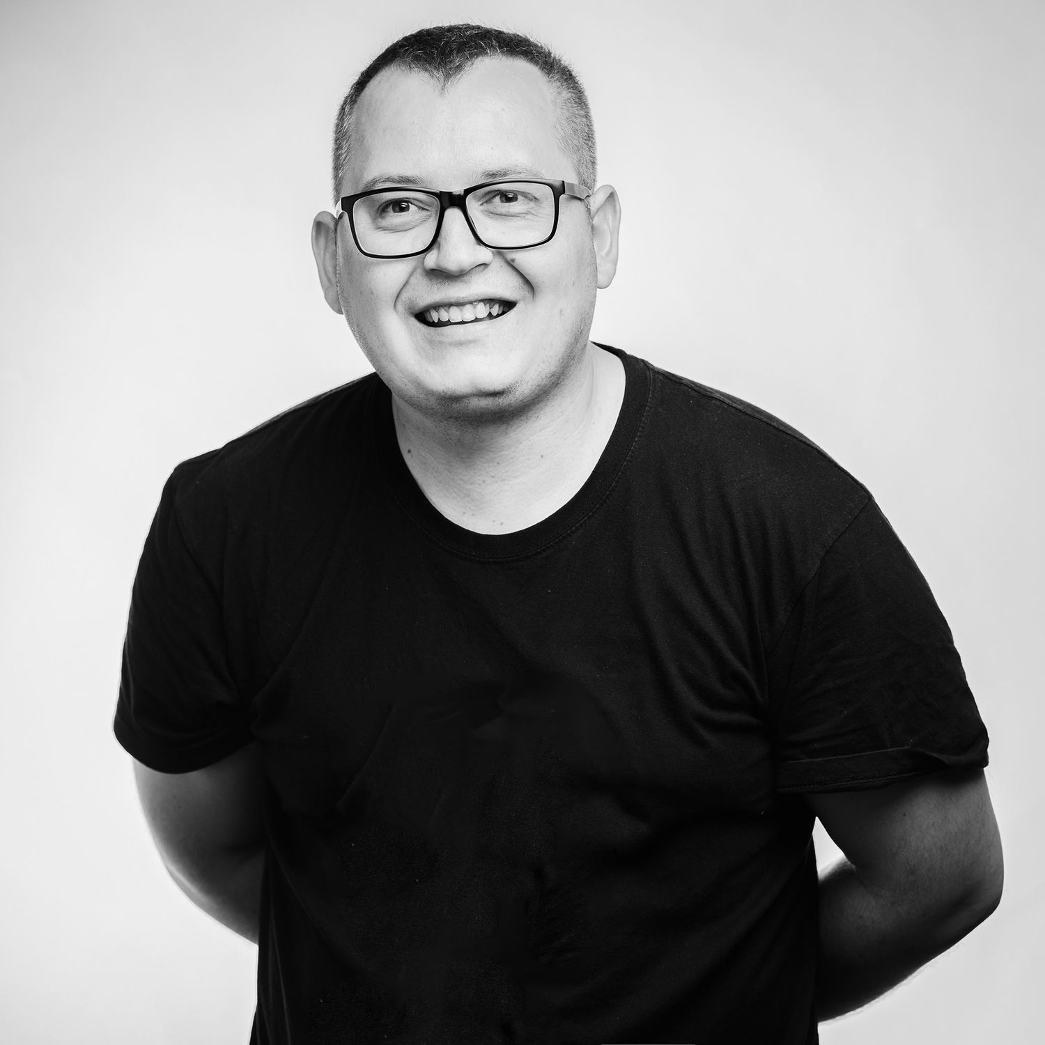 Black and white professional headshot of someone wearing glasses and a black t-shirt with a cheerful expression.