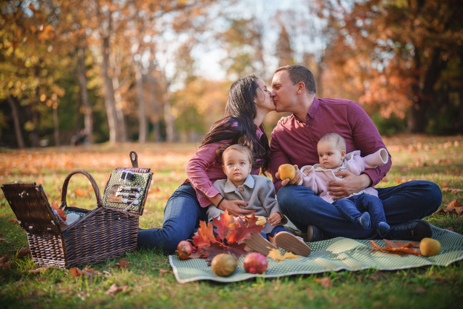 Family having an autumn picnic with a basket and blanket surrounded by fall foliage.
