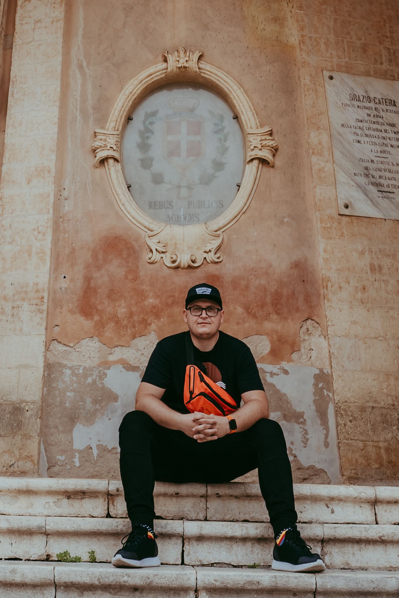 Someone in casual black attire sitting on stone steps beneath an ornate architectural frame.