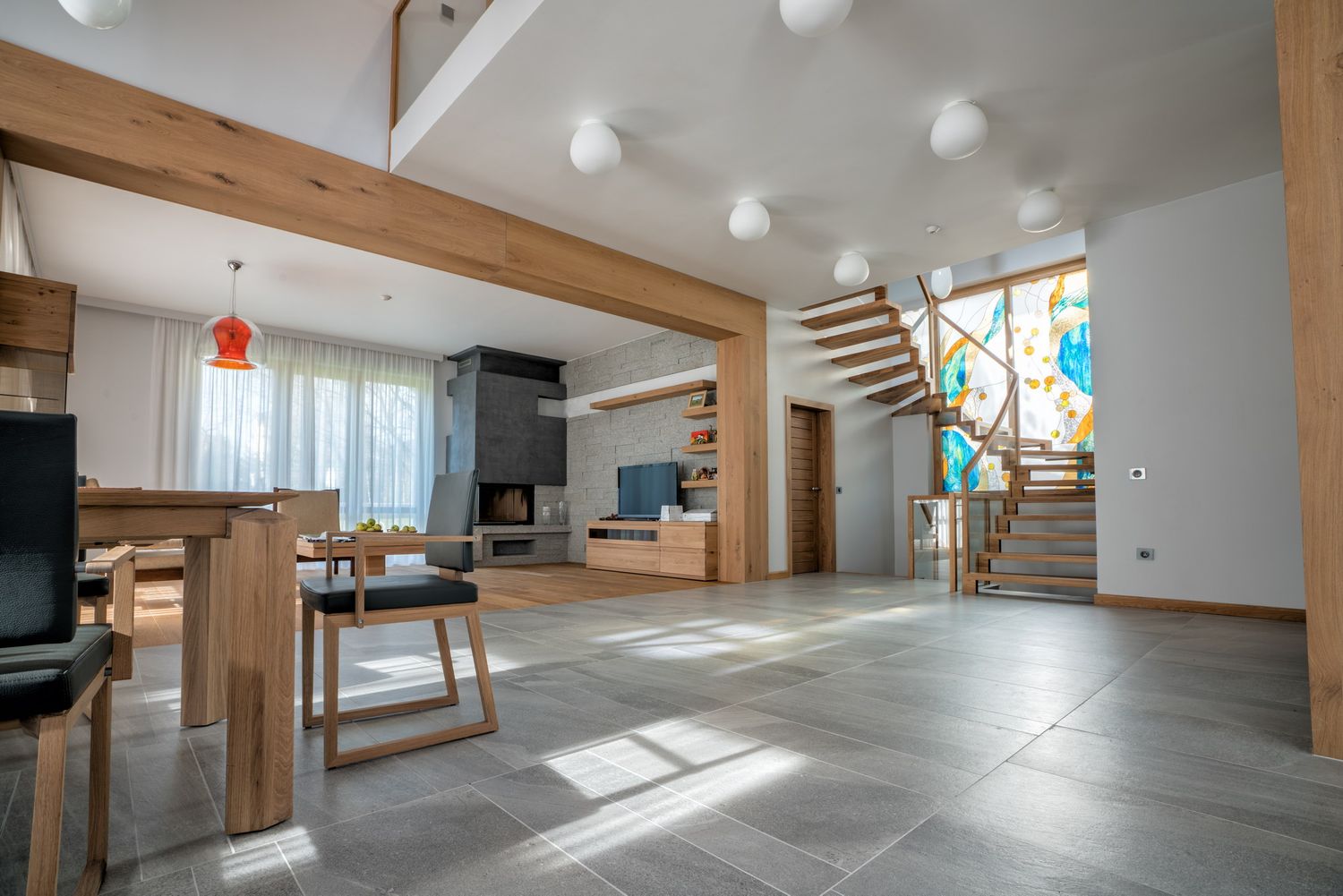 Bright open-plan living space with wooden beams, white ceiling lights, and modern staircase design.