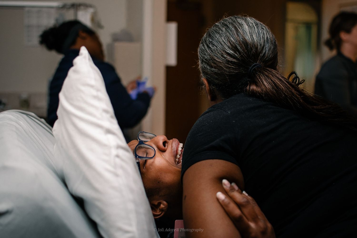 Woman With Glasses Lying On A Pillow Crying In Labor Holding Woman's Arm