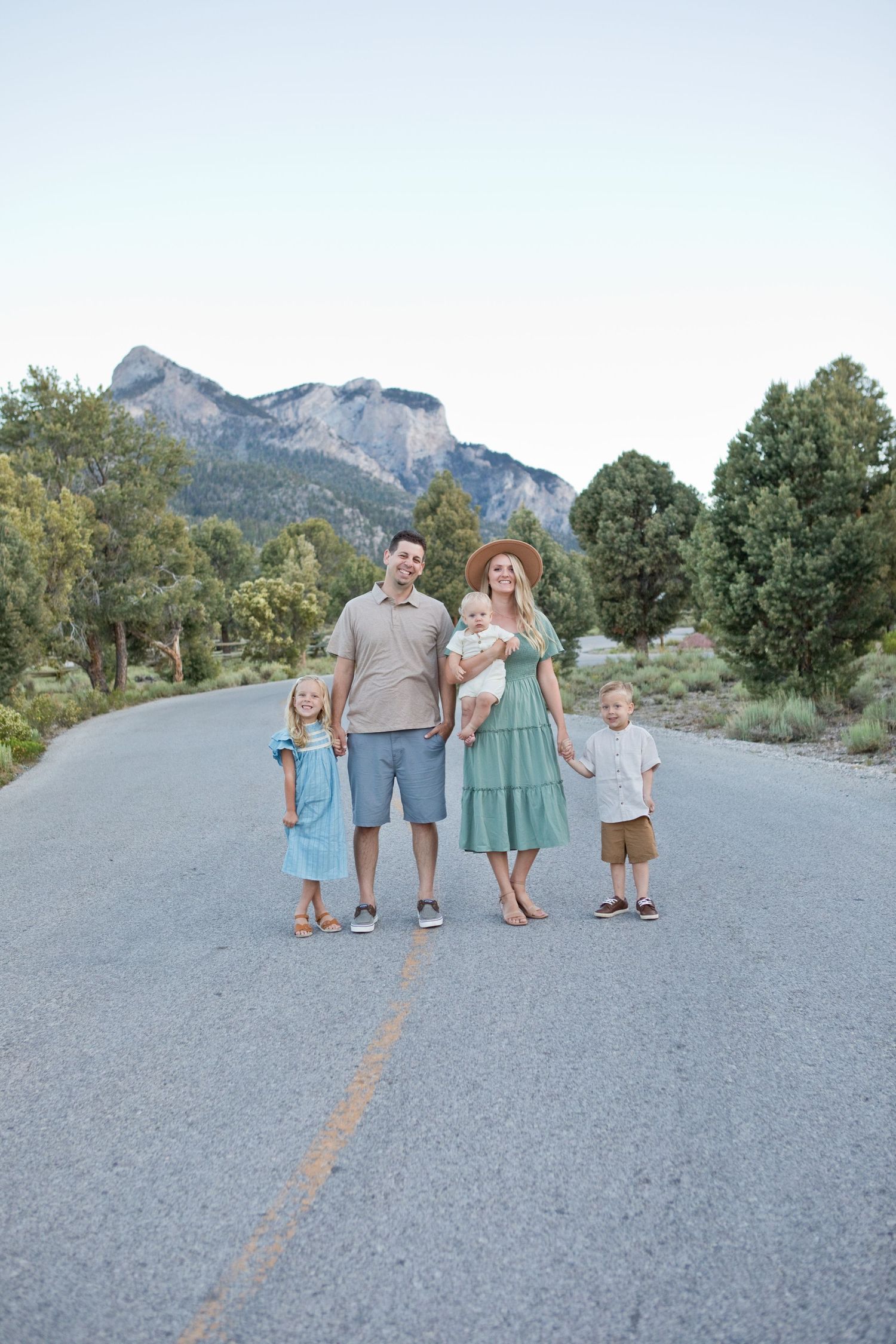 A family standing on a mountain road with scenic peaks in the background.
