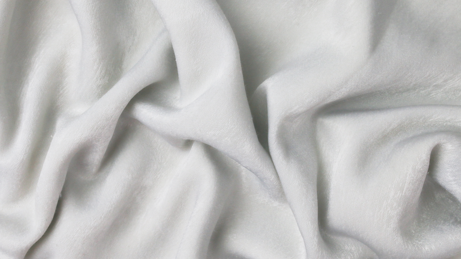 Close-up texture of flowing white fabric with soft folds and creases.