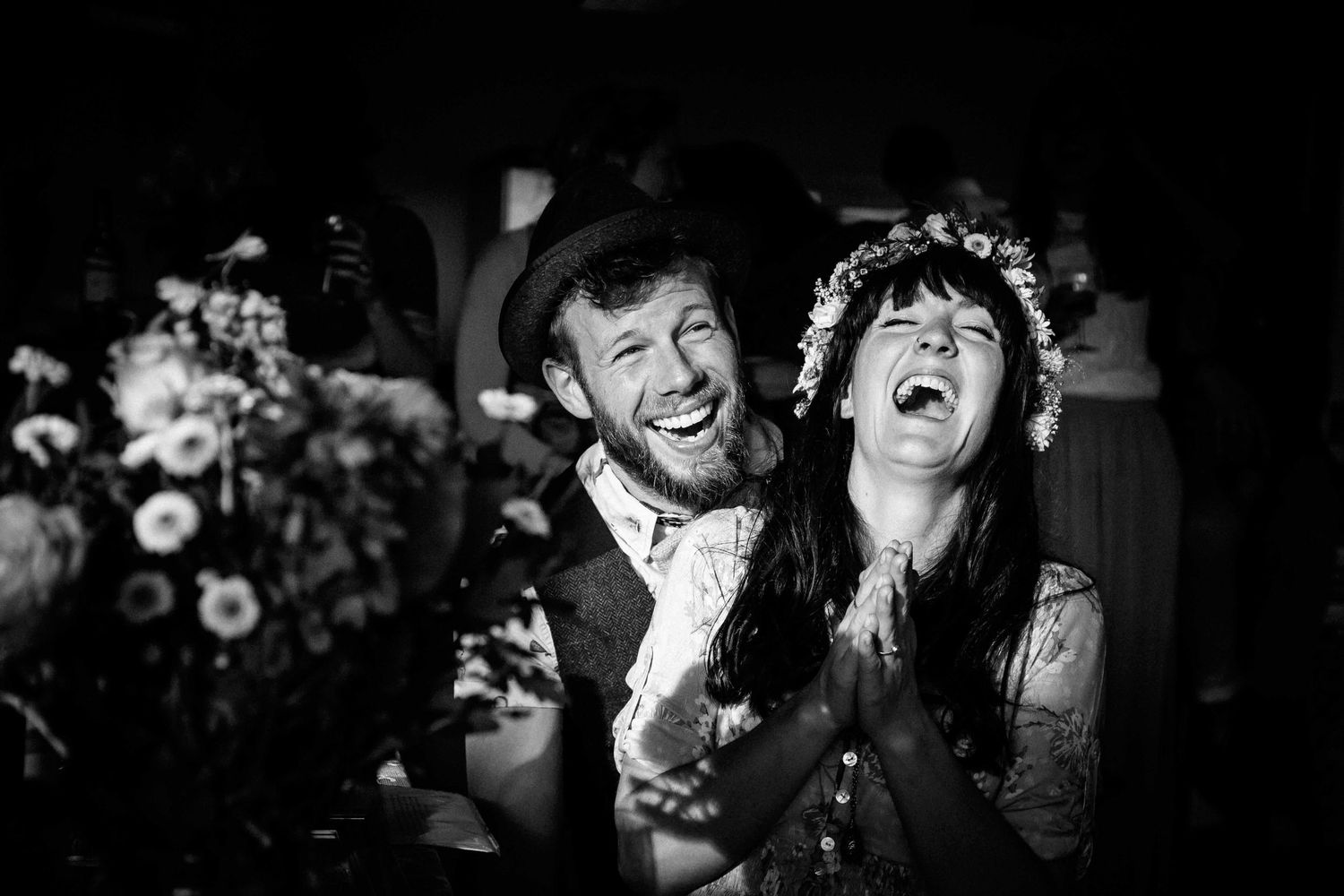 A groom sits behind his bride as they laugh ecstatically together surrounded by beautiful flowers