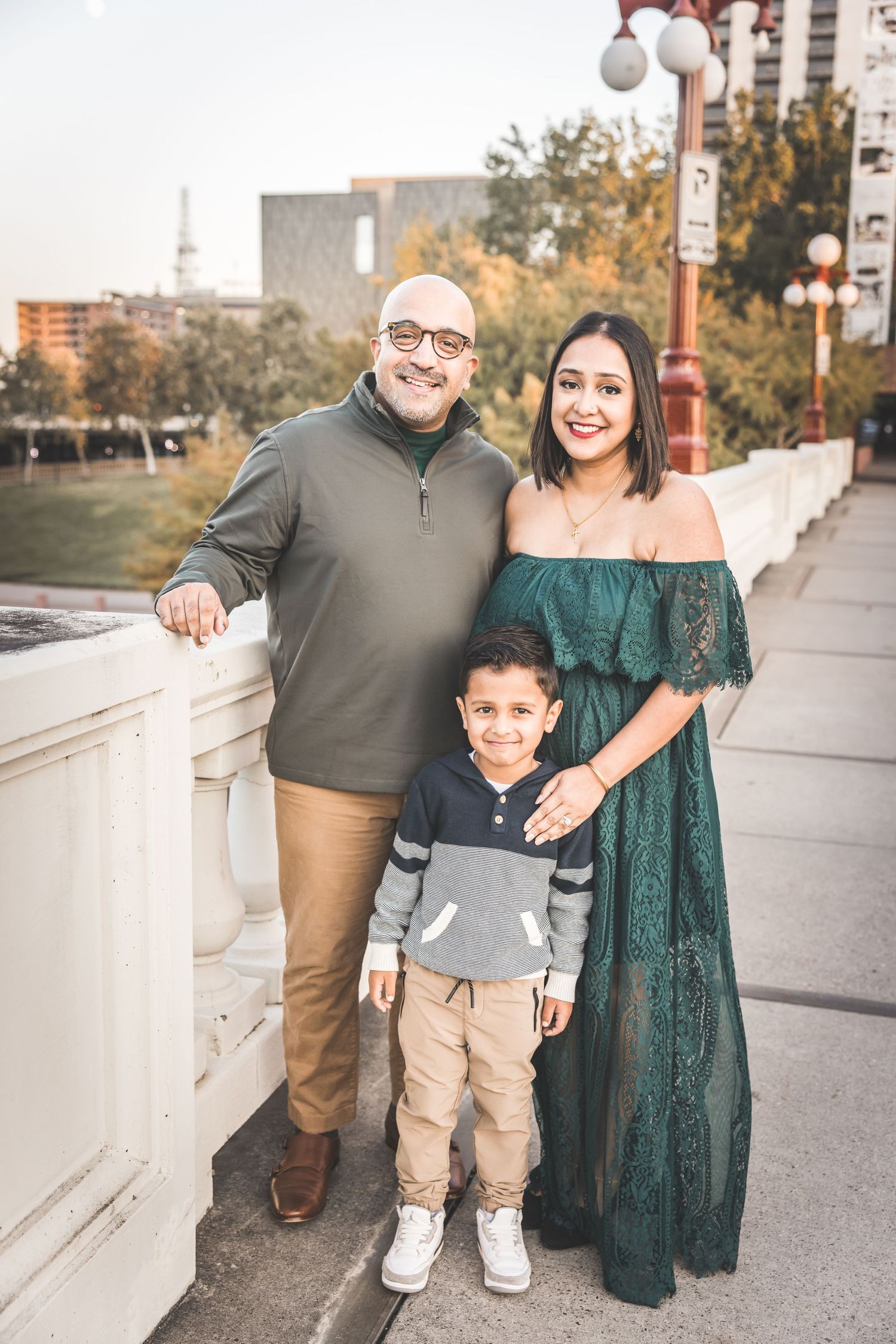 A family poses together outdoors on a sunny autumn day wearing coordinated outfits in green and neutral tones.  Houston Family Photographer