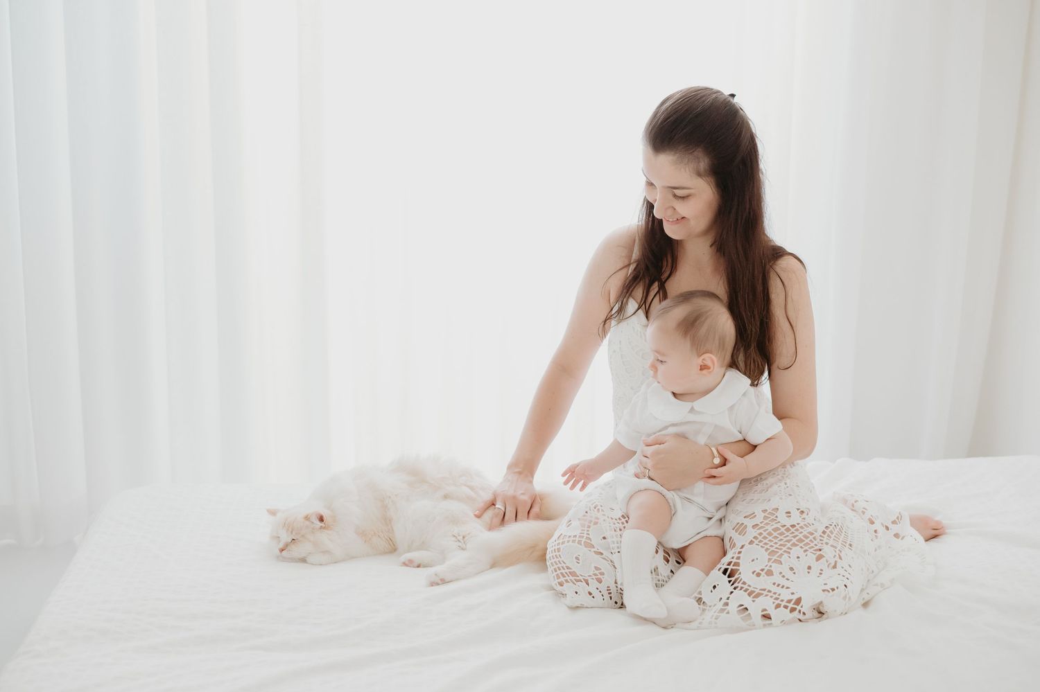 Tender moment on white bedding with baby in soft lighting.
