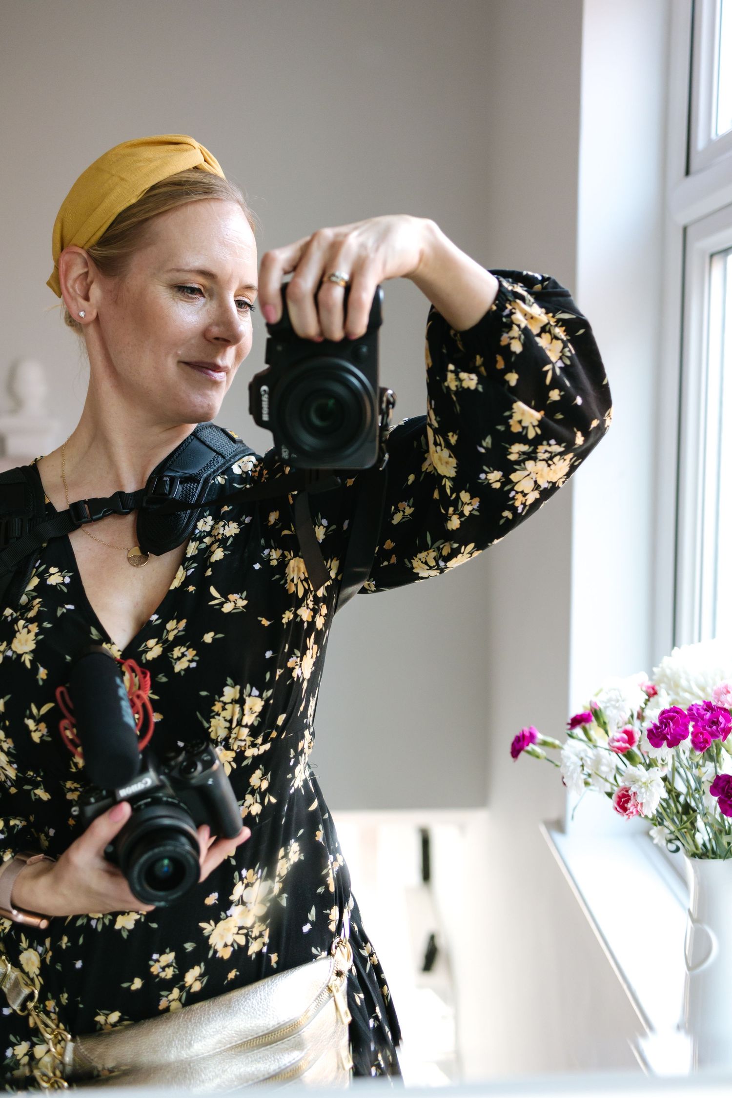 Photographer in floral dress and yellow headband taking a self-portrait with professional camera.