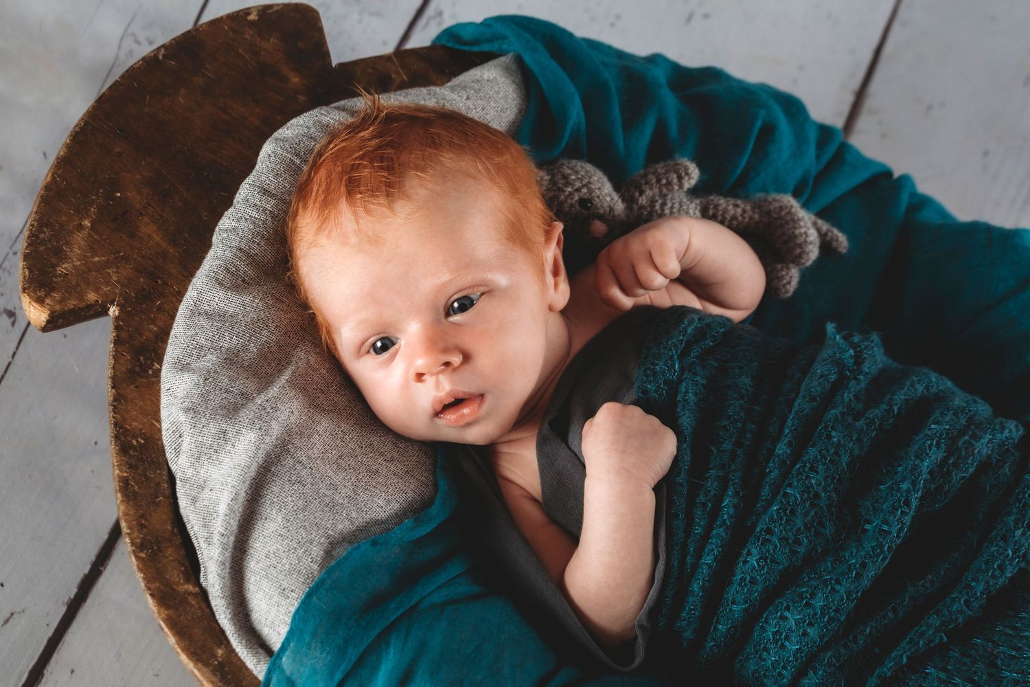Infant lying on teal blanket with stuffed animal looking up at camera.