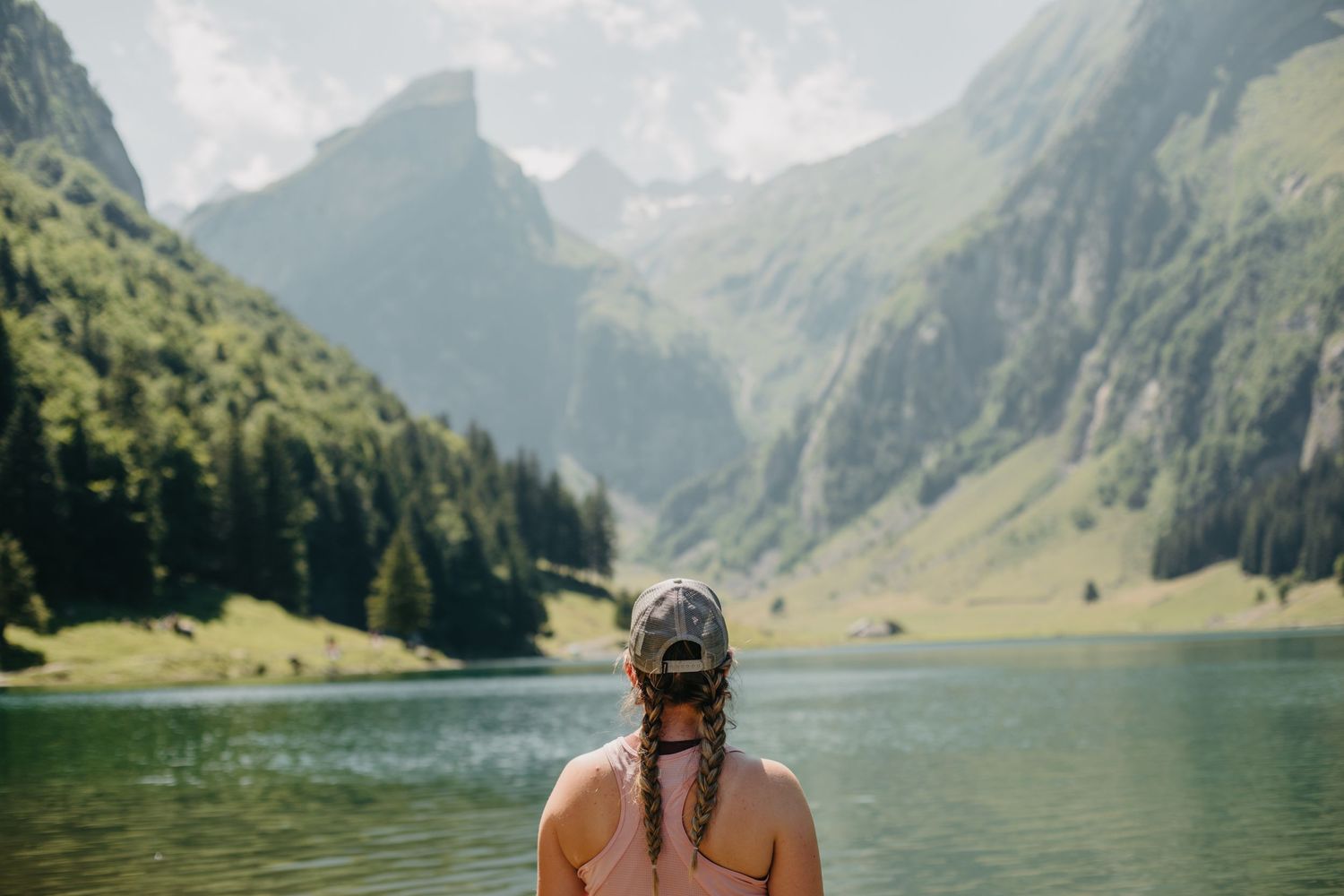 Person with braided hair looking out at a serene mountain lake landscape.