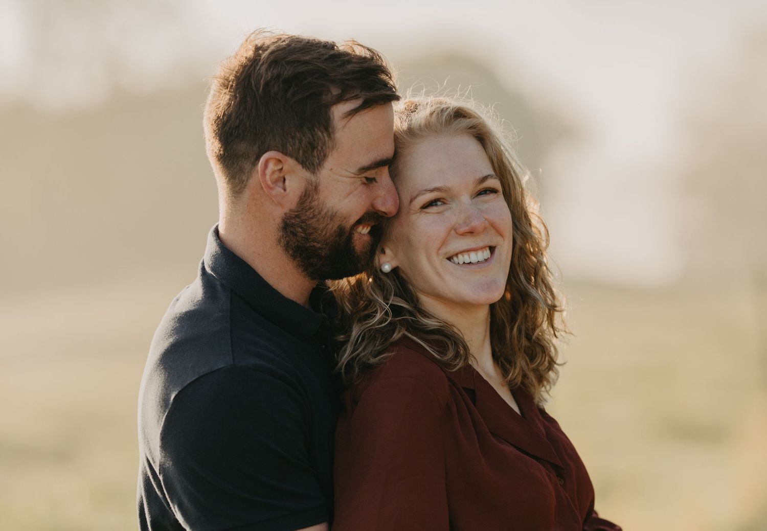Candid portrait of a loving couple laughing together during golden hour in a natural setting.