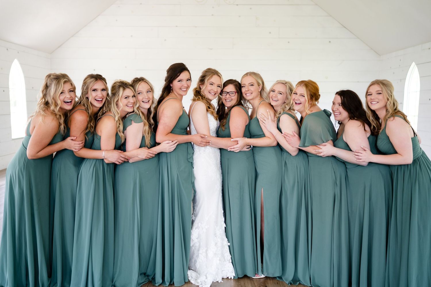 Wedding party wearing matching sage green bridesmaid dresses lined up in elegant pose.