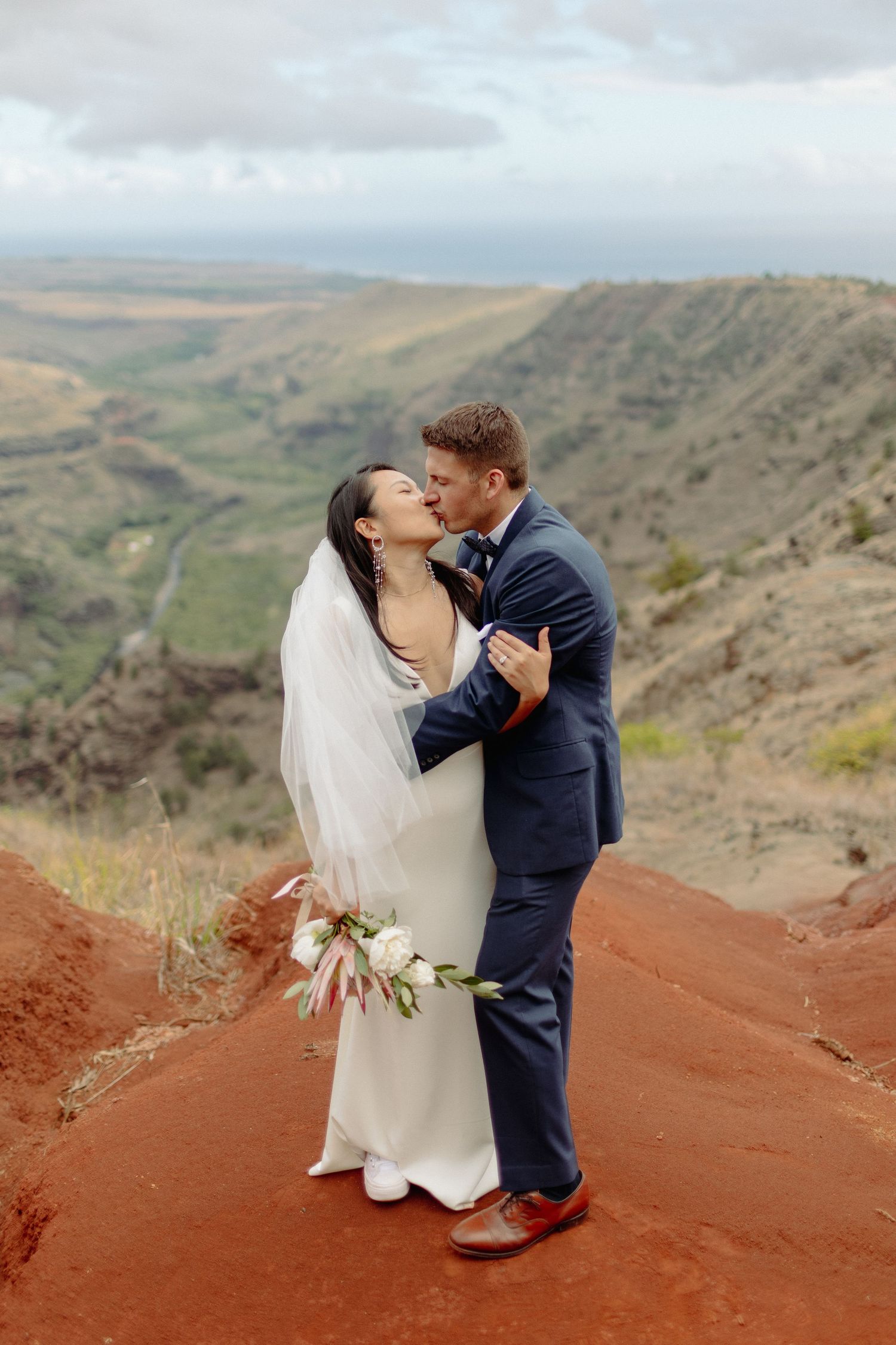 a bride and groom kiss amongst the red ocre dirt in kauai before their wedding