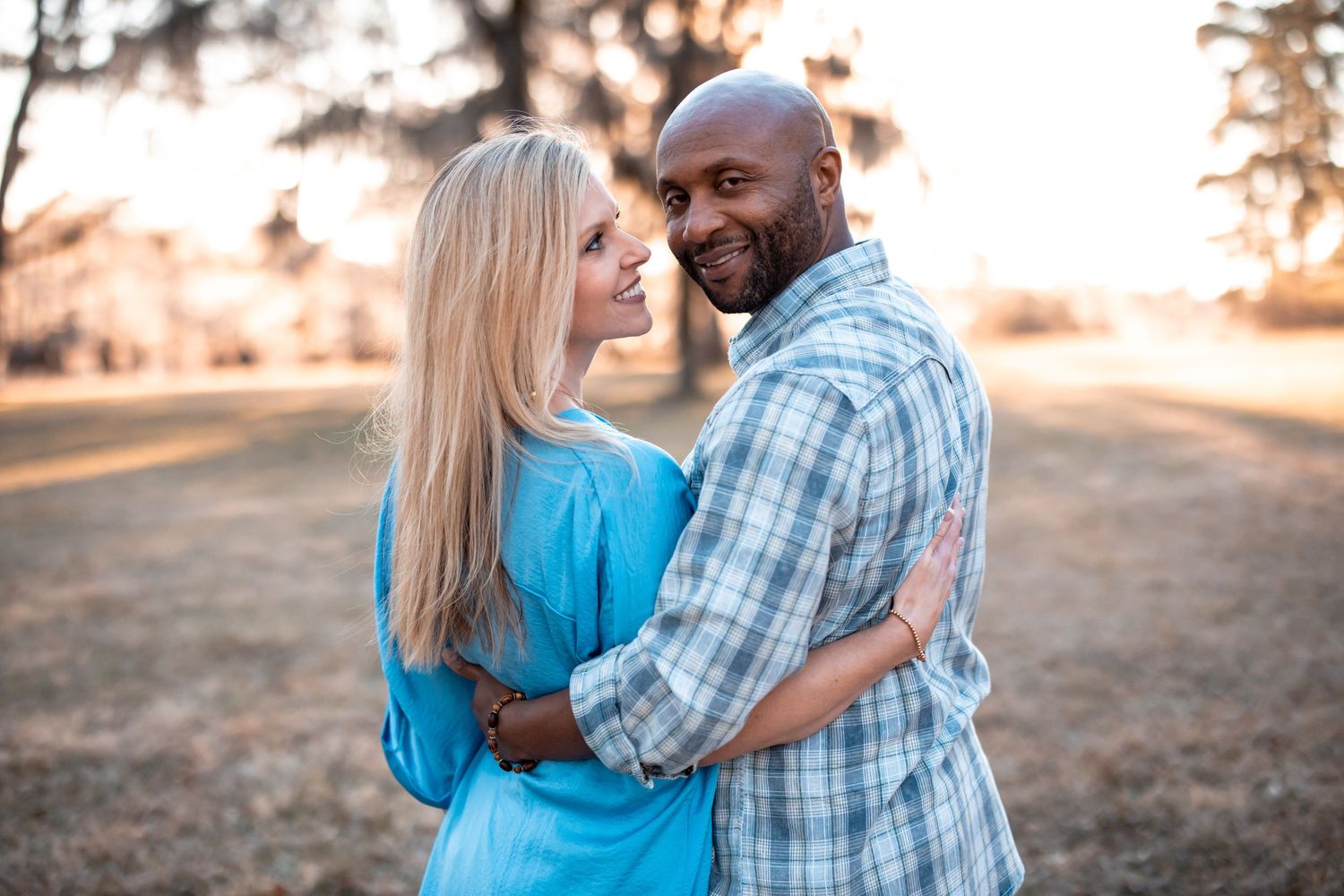 A couple embraces during a romantic sunset photoshoot in casual attire.