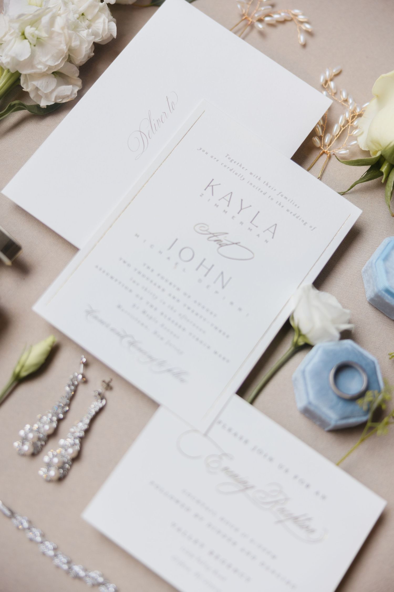 Elegant wedding invitation suite for Kayla and John with pearl earrings and blue ring box on neutral background.