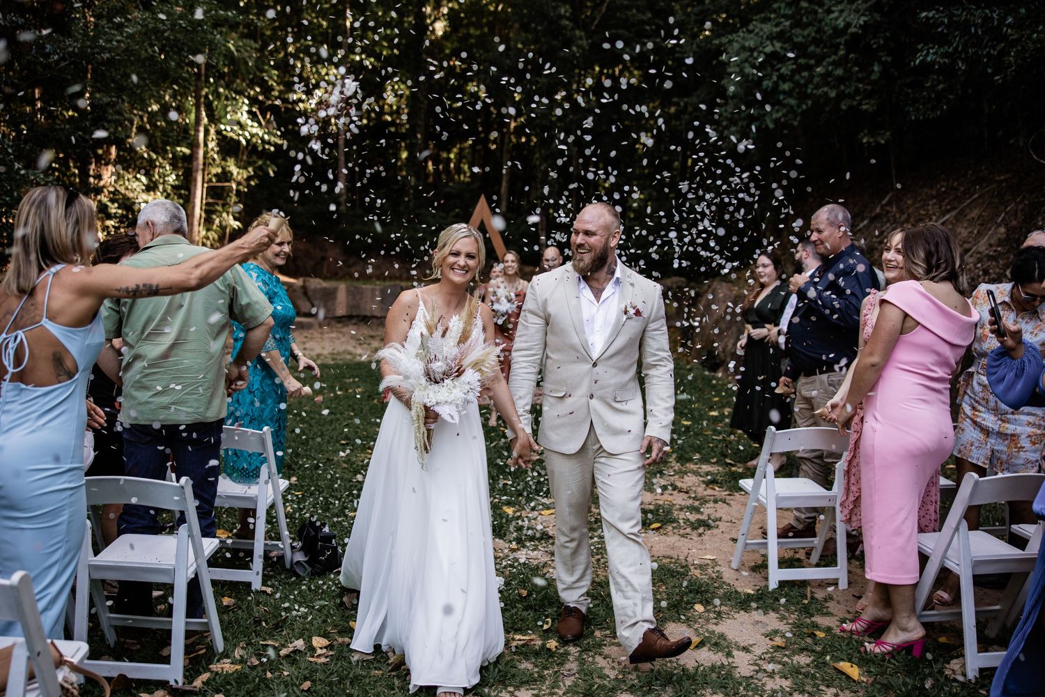 A celebratory moment at an outdoor wedding with guests throwing confetti in a garden setting.